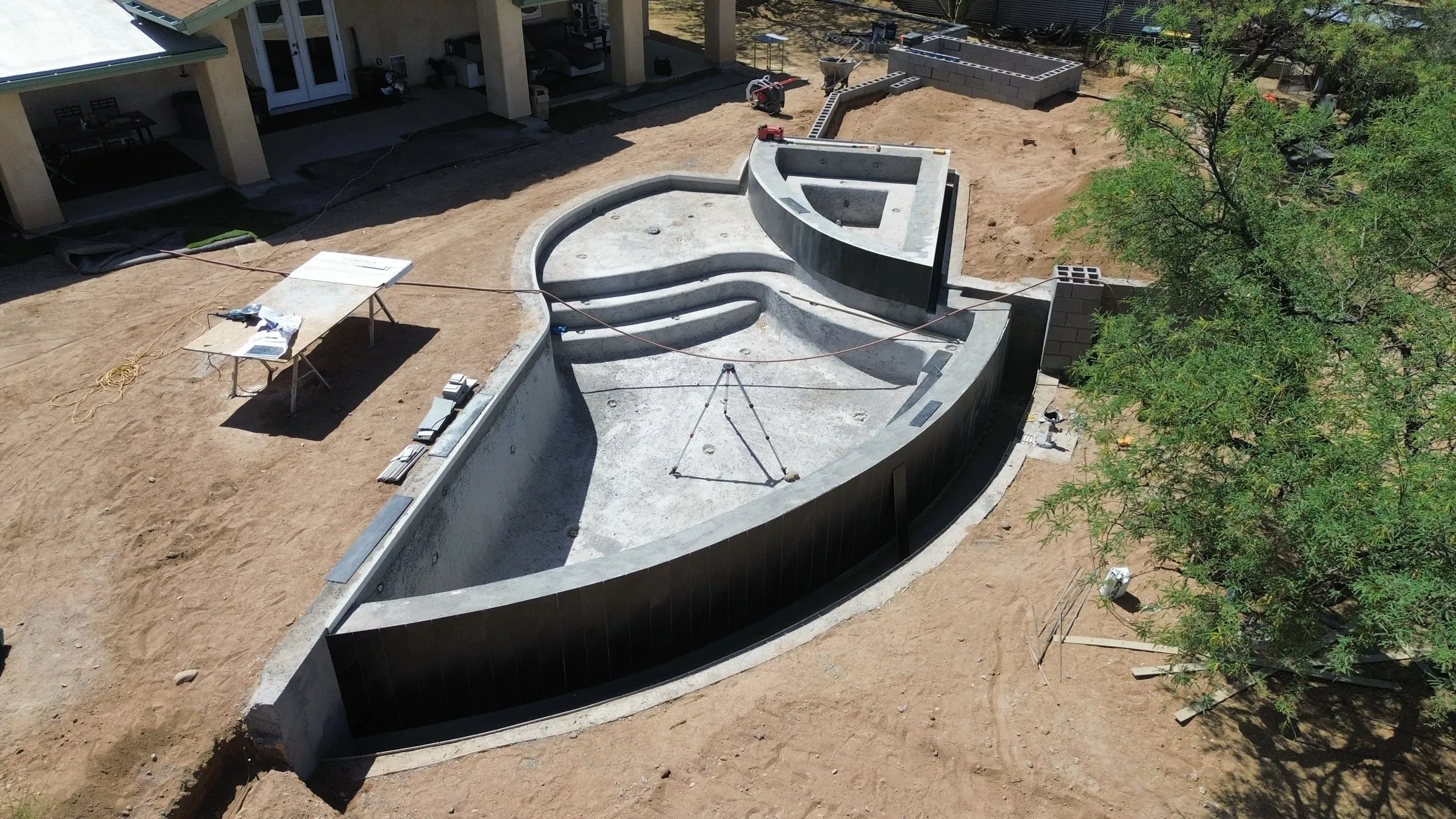 Aerial view of a curved vanishing-edge pool shell, entry steps and spa before tile