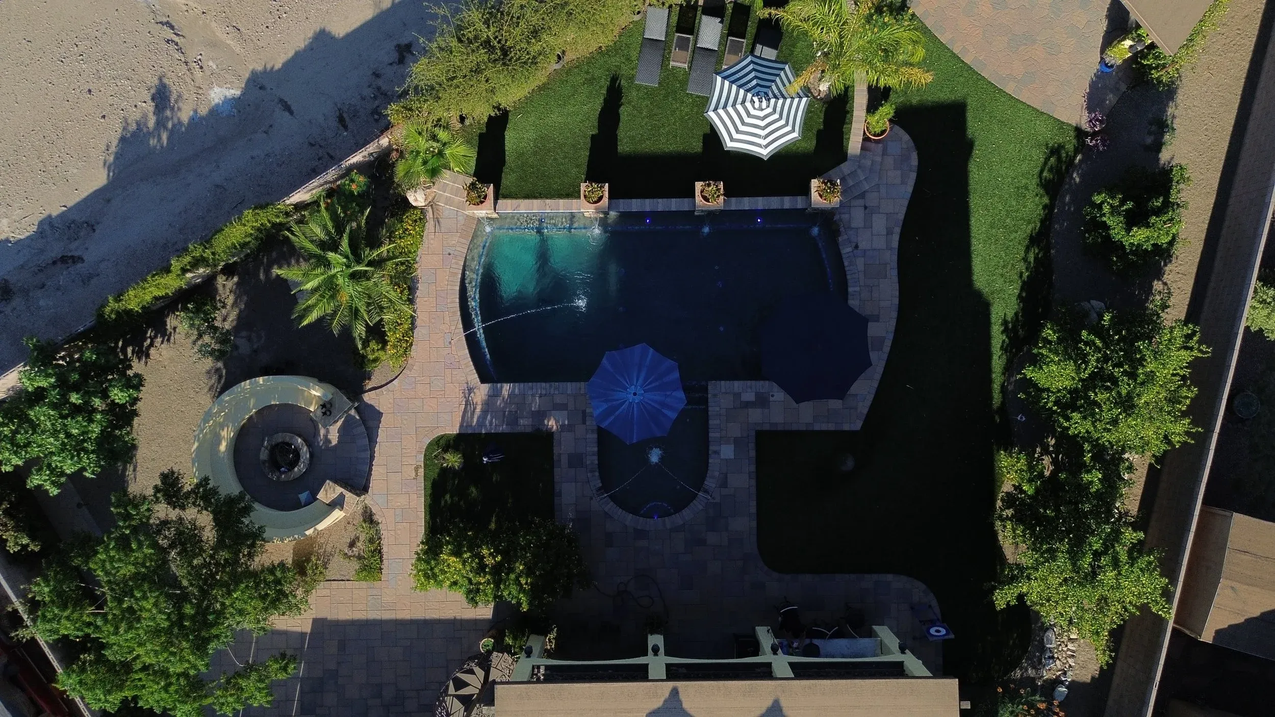 Aerial view of a freeform pool with paver deck, fire pit and turf