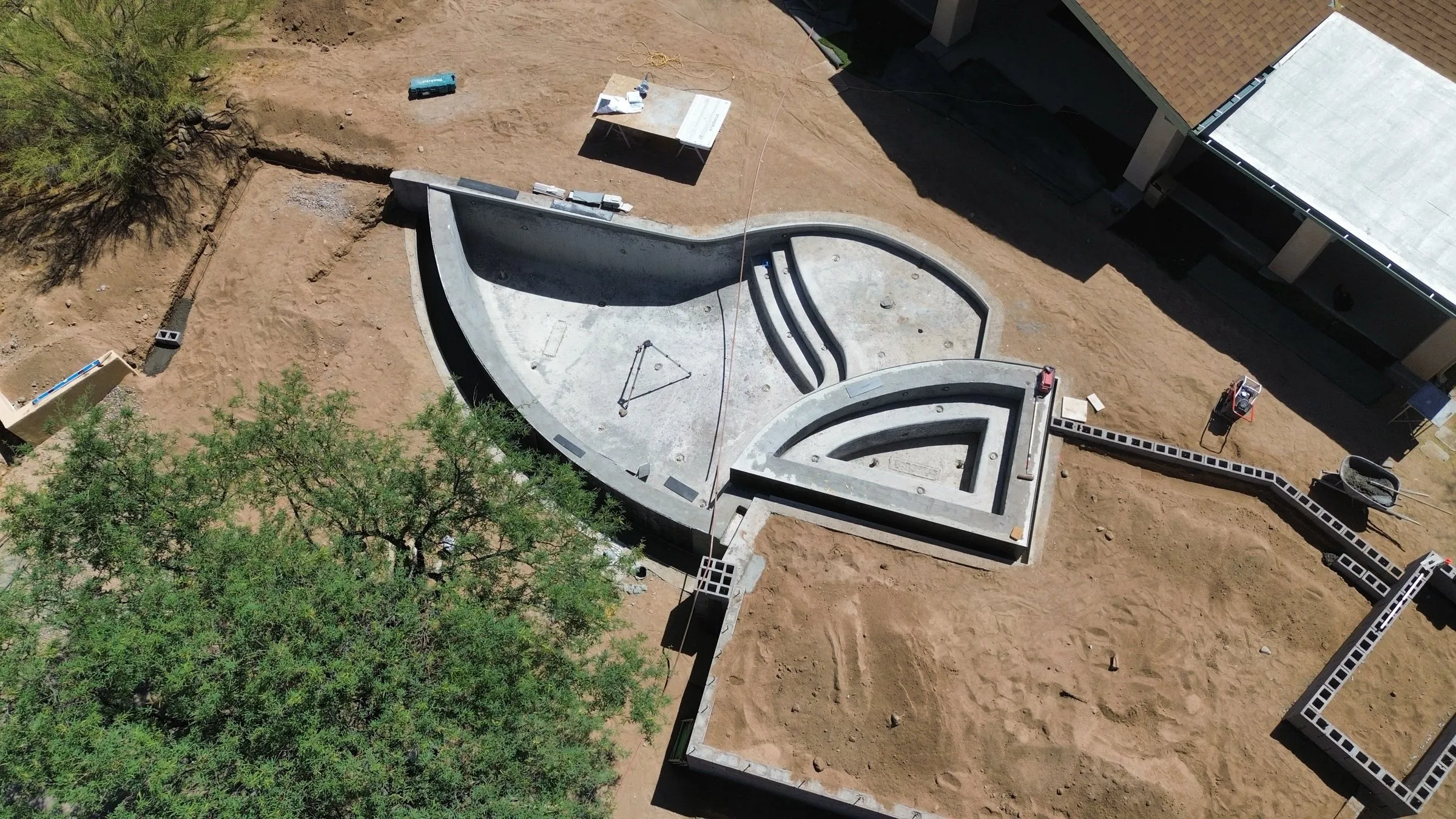 Drone view of a freeform infinity-edge pool shell with a raised spa and new block walls