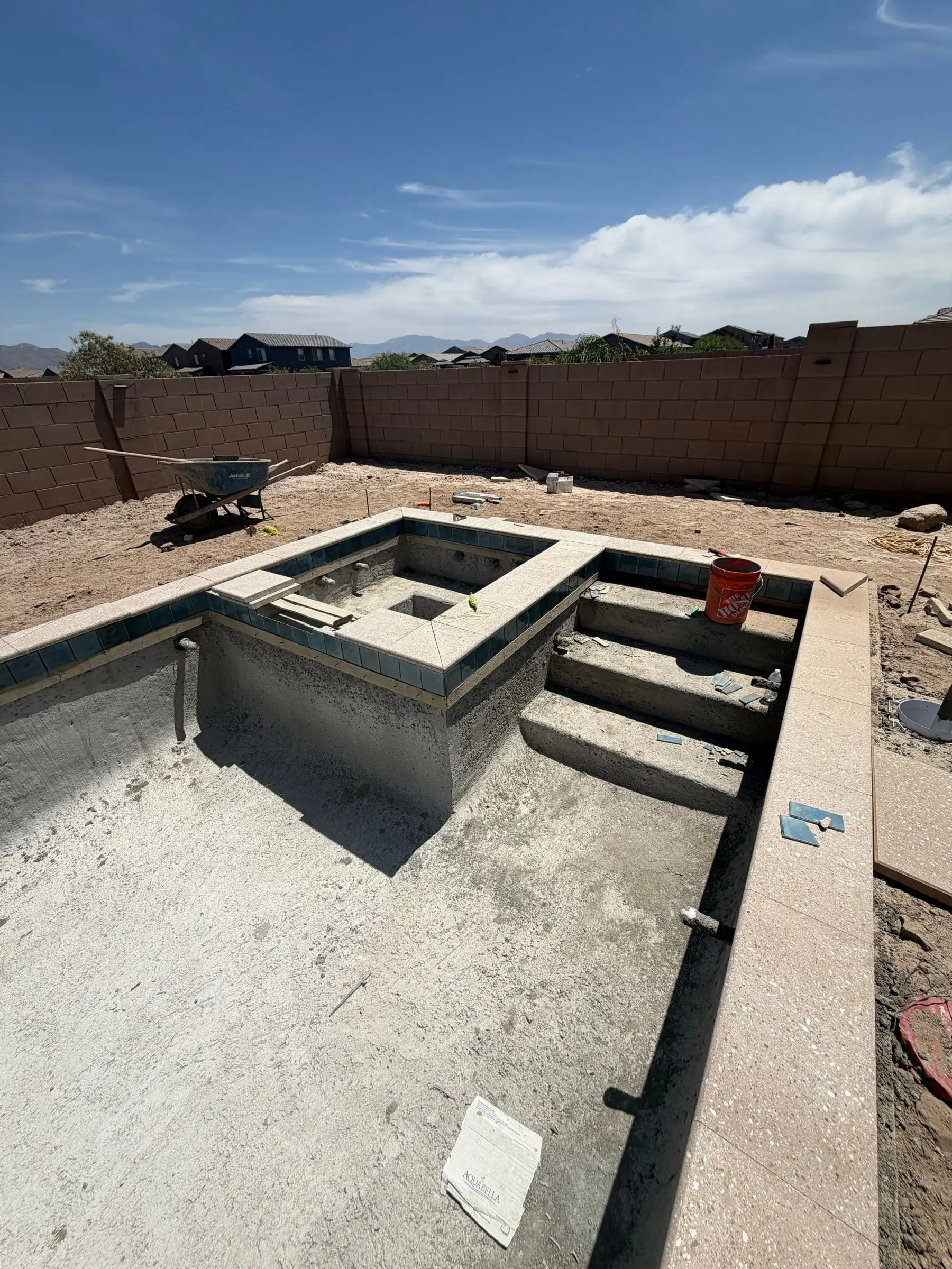 Shotcrete shell of a square spa attached inside the corner of a new pool, with entry steps.
