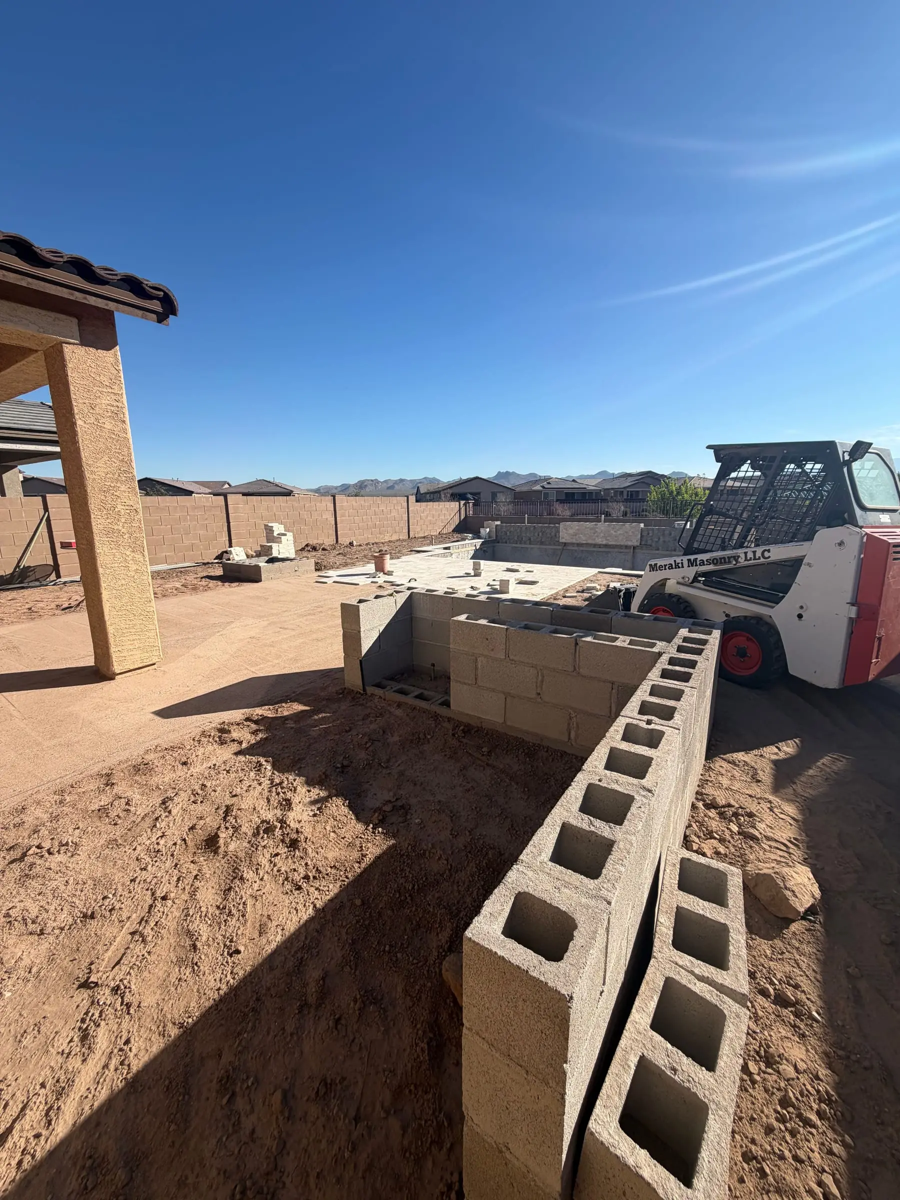 Concrete block raised wall going up beside a new pool, with a skid steer working in the yard, Marana, AZ.
