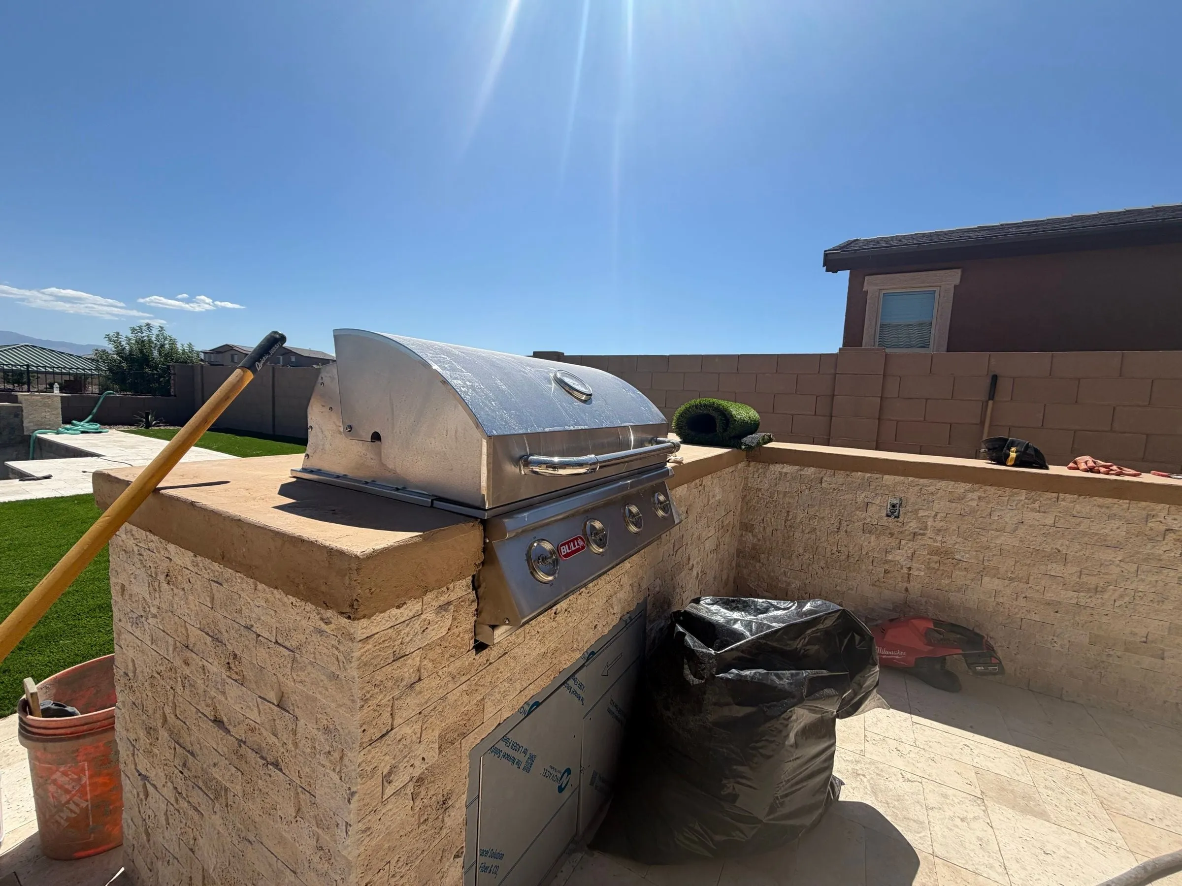 Built-in stainless grill in a stacked stone island being finished beside the pool deck.