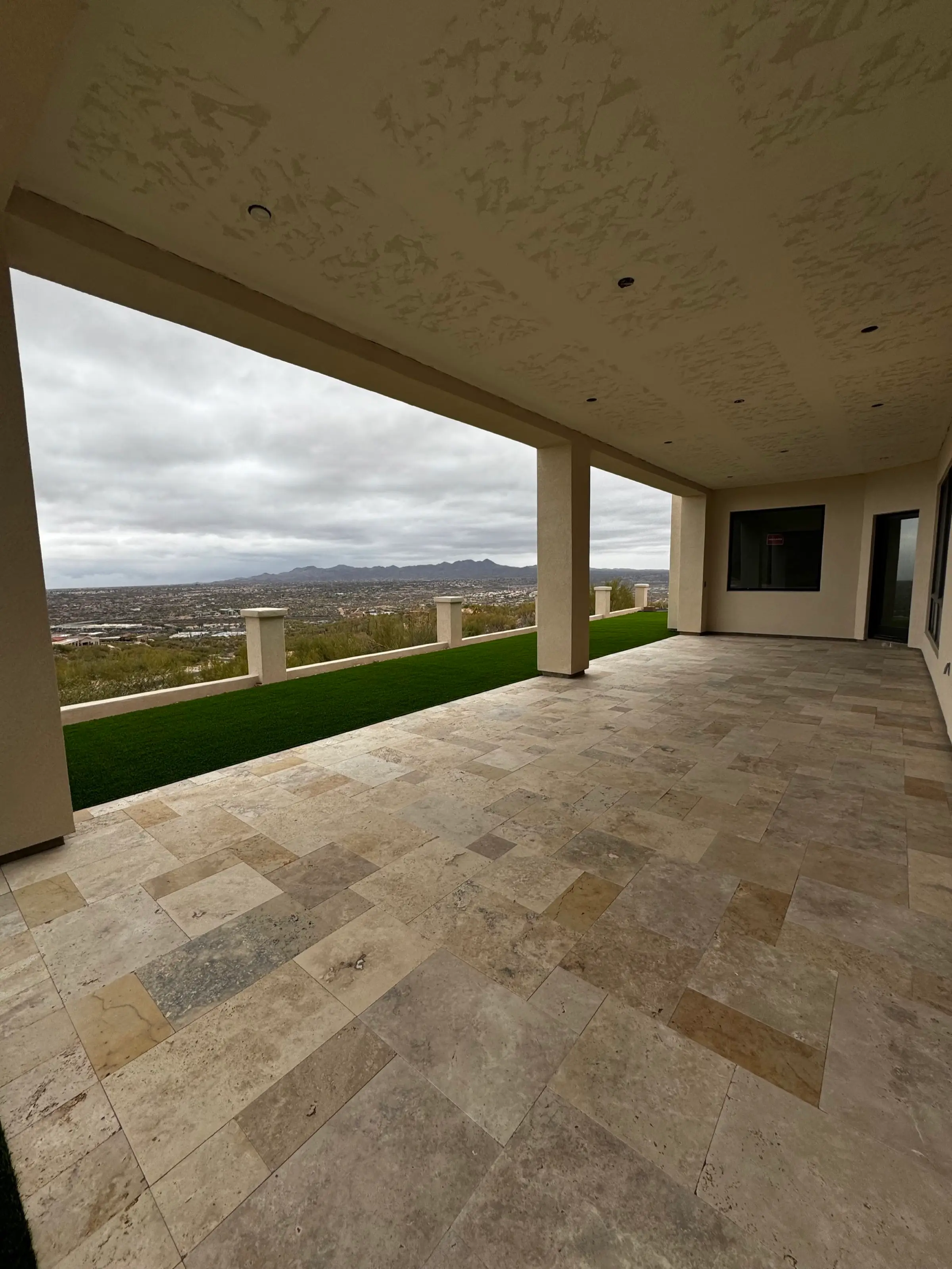 Covered patio with travertine flooring and artificial turf overlooking a valley and distant mountains.