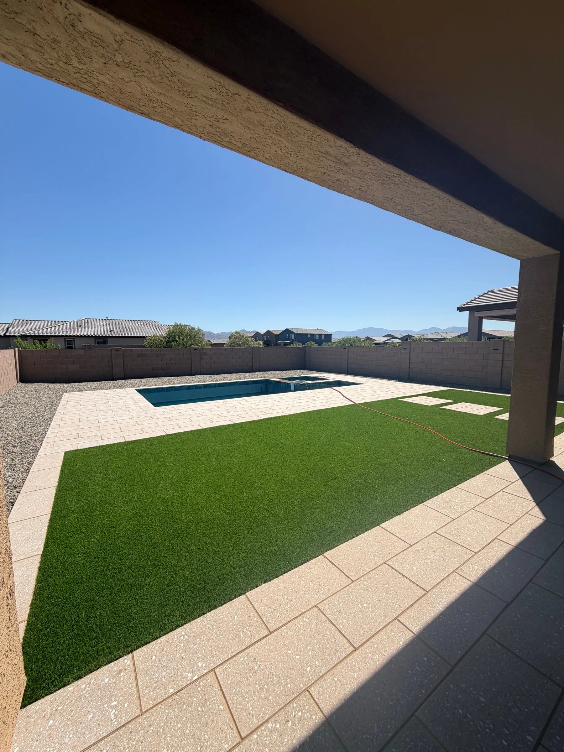 View from a covered patio across artificial turf and paver deck to the finished pool