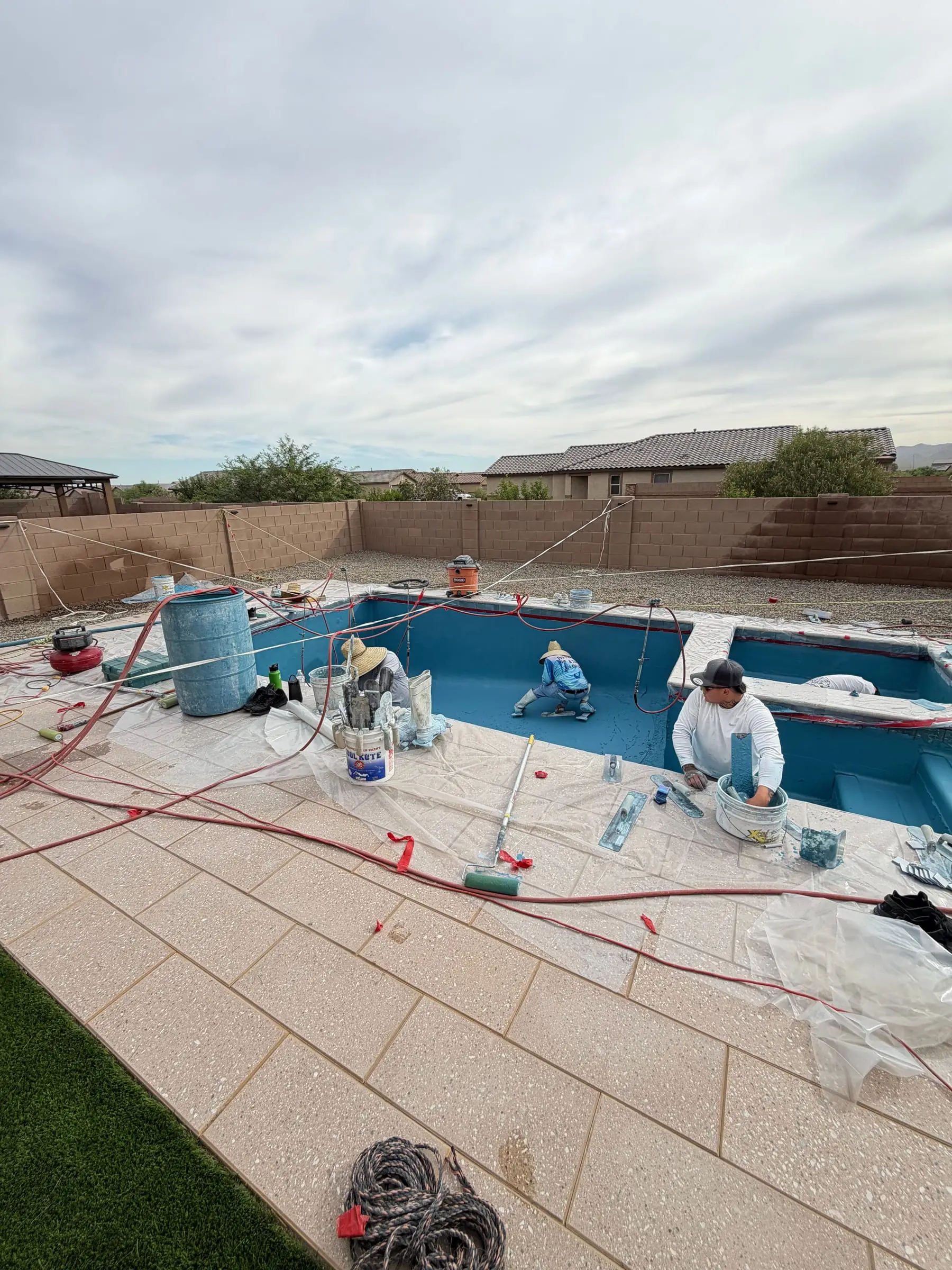 Our crew applying the interior finish to a new pool and spa, with the paver deck covered for protection, Gladden Farms in Marana, AZ.