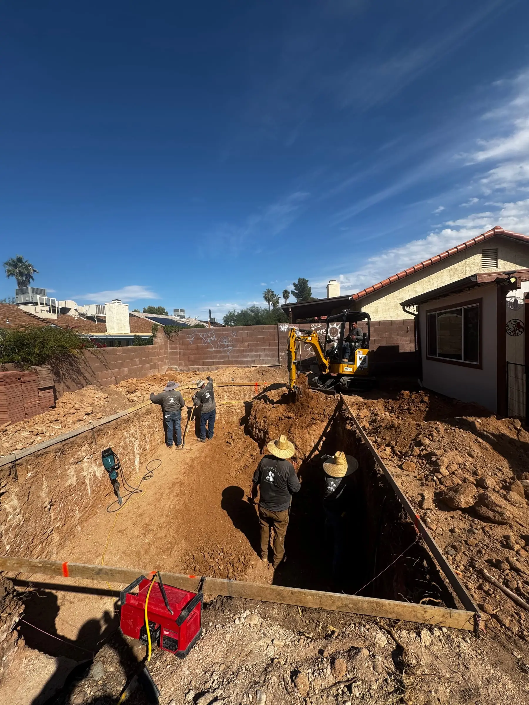Our crew digging a pool with a mini excavator between block walls.