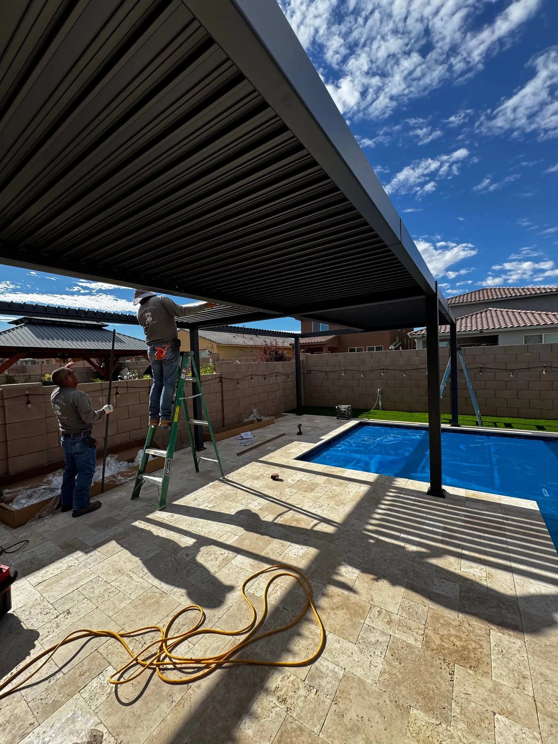 Our crew installing a louvered pergola over a travertine pool deck, set on concrete footings beside a new pool in southeast Tucson.