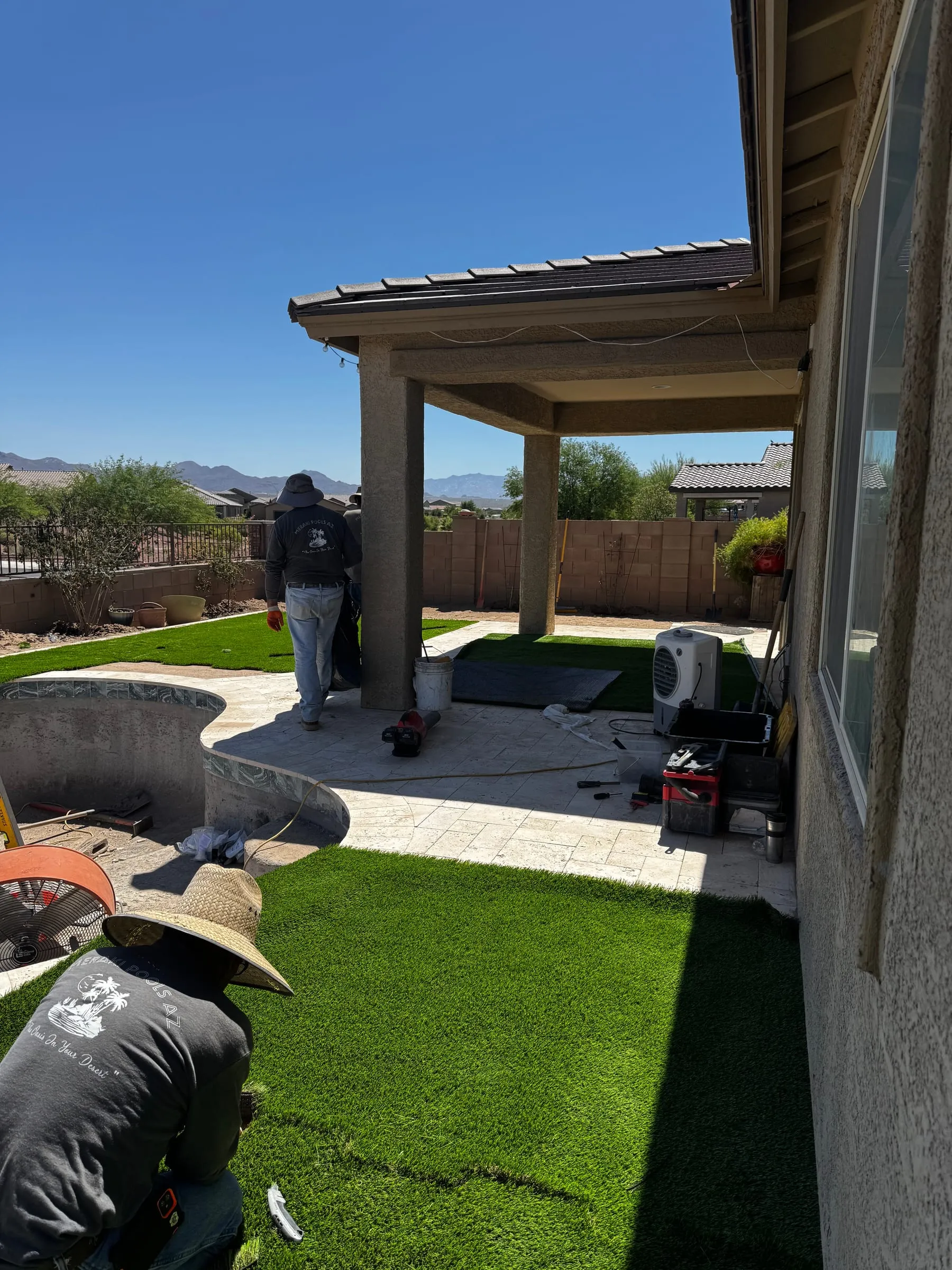 Crew installing artificial turf around a new freeform pool and travertine patio in Marana.