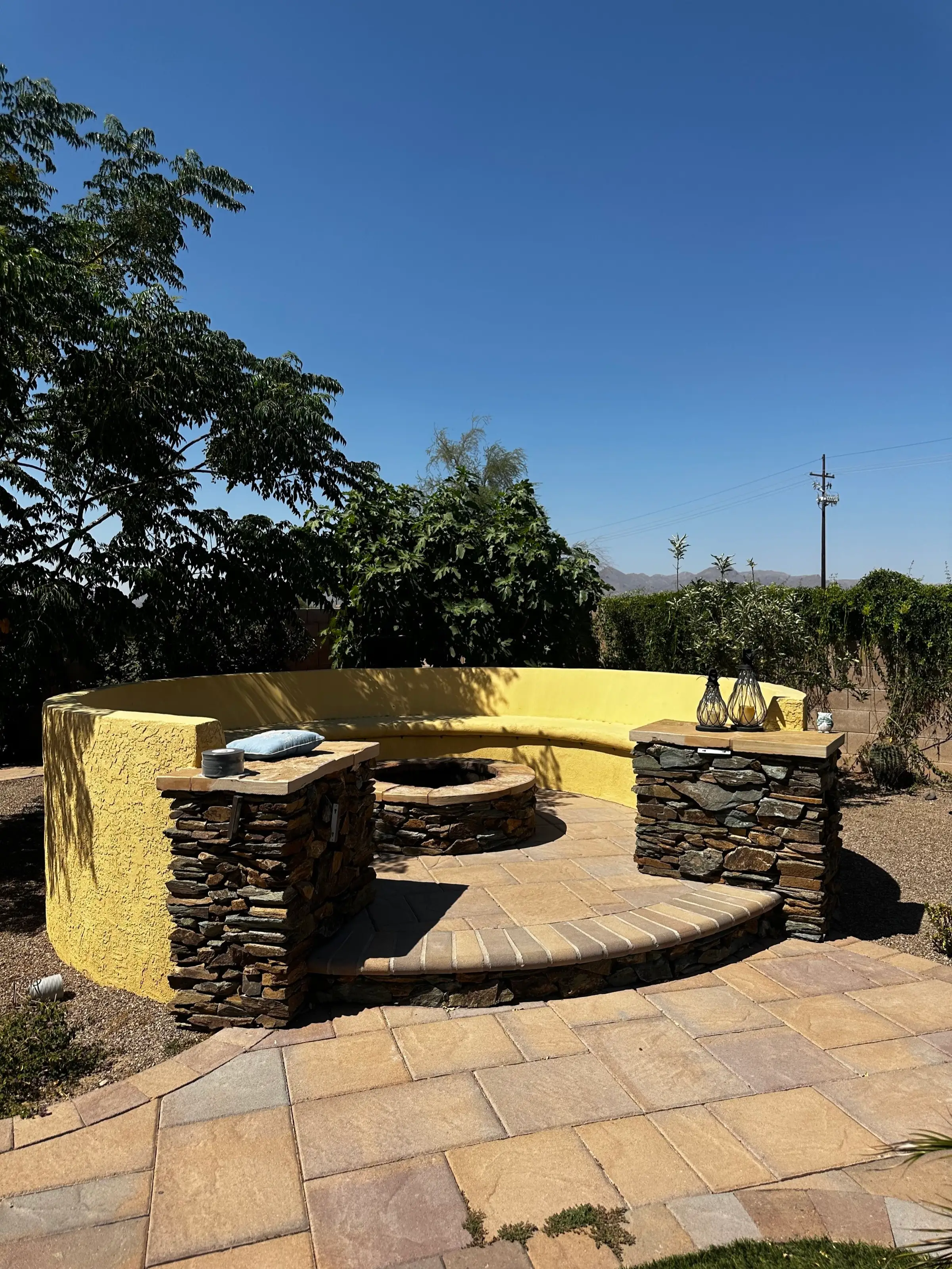 Curved built-in bench with stacked stone pillars around a fire pit on a paver patio.