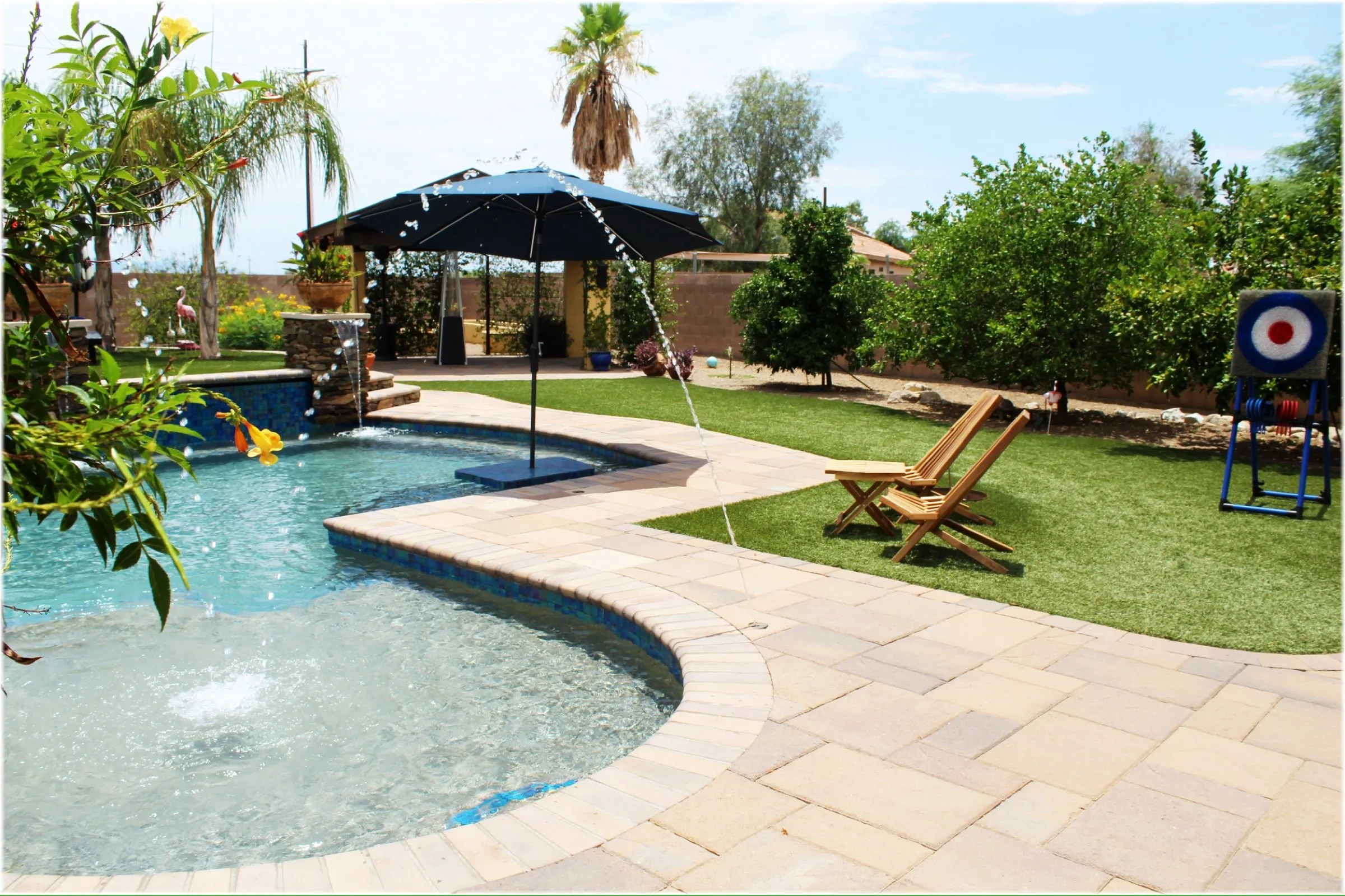 Curving paver coping wraps a tanning ledge with bubbler beside a grass lawn and shade umbrella