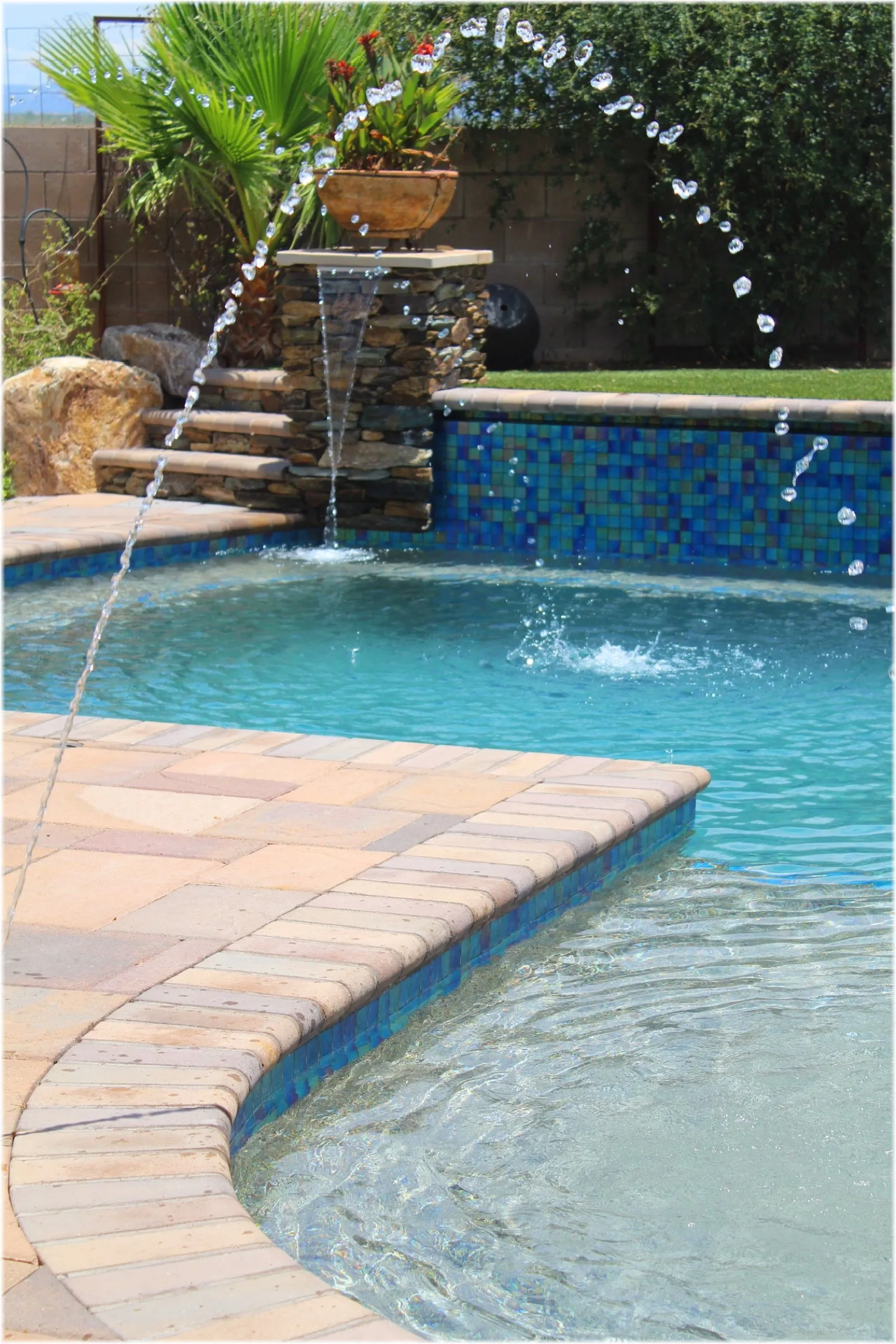 Arcing deck jets and a stacked stone sheer descent over a blue glass tile wall
