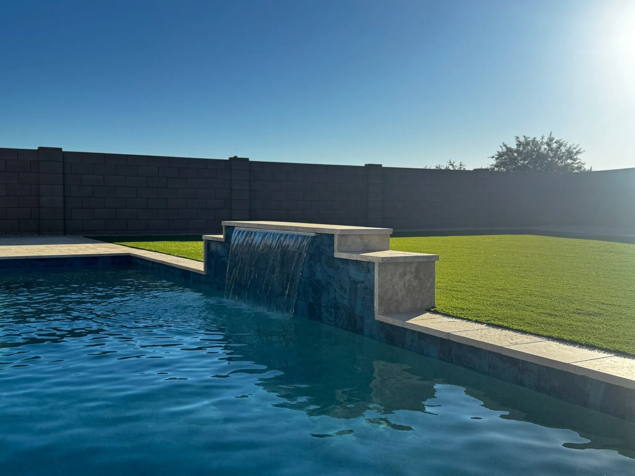 Low-maintenance modern pool with a stone water wall and artificial turf