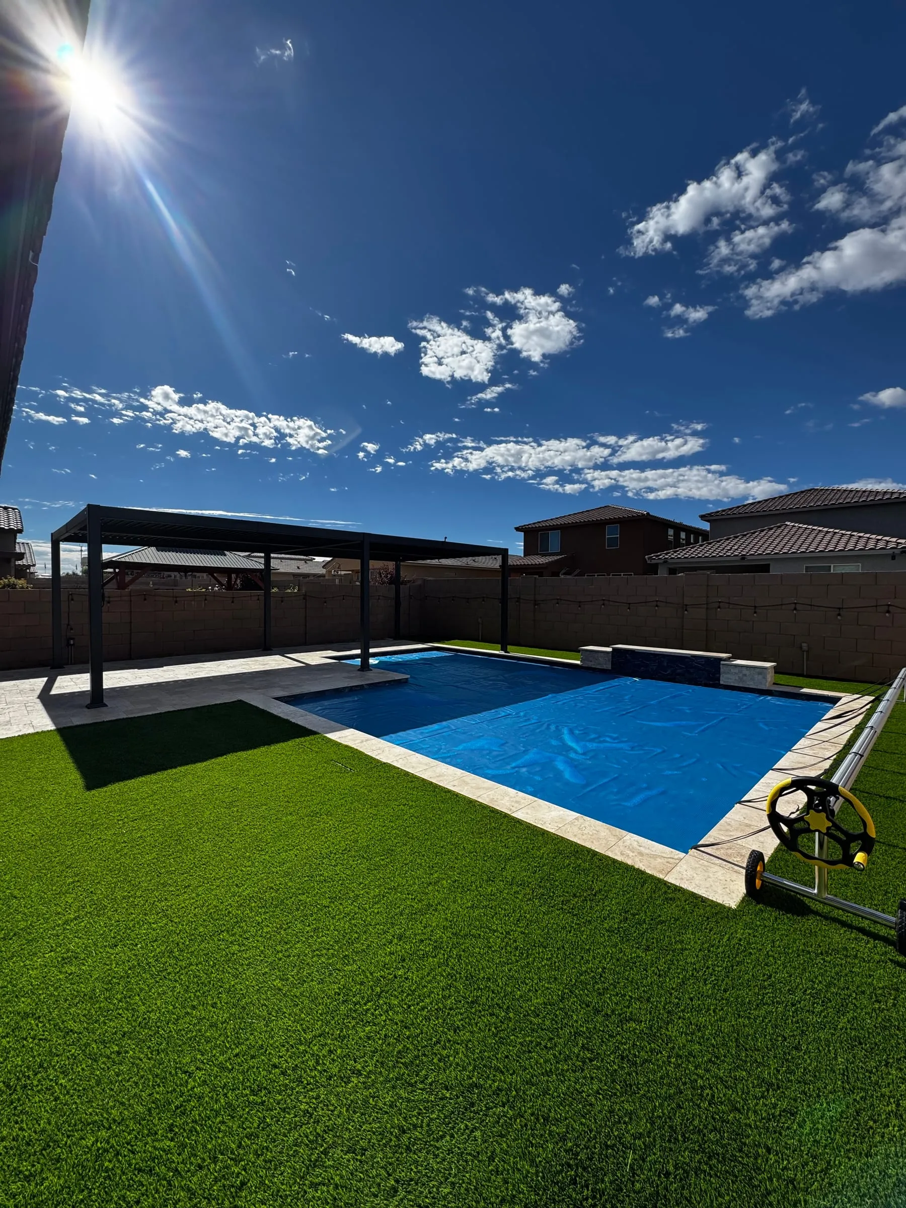 Finished pool under a solar cover, framed by travertine and turf.