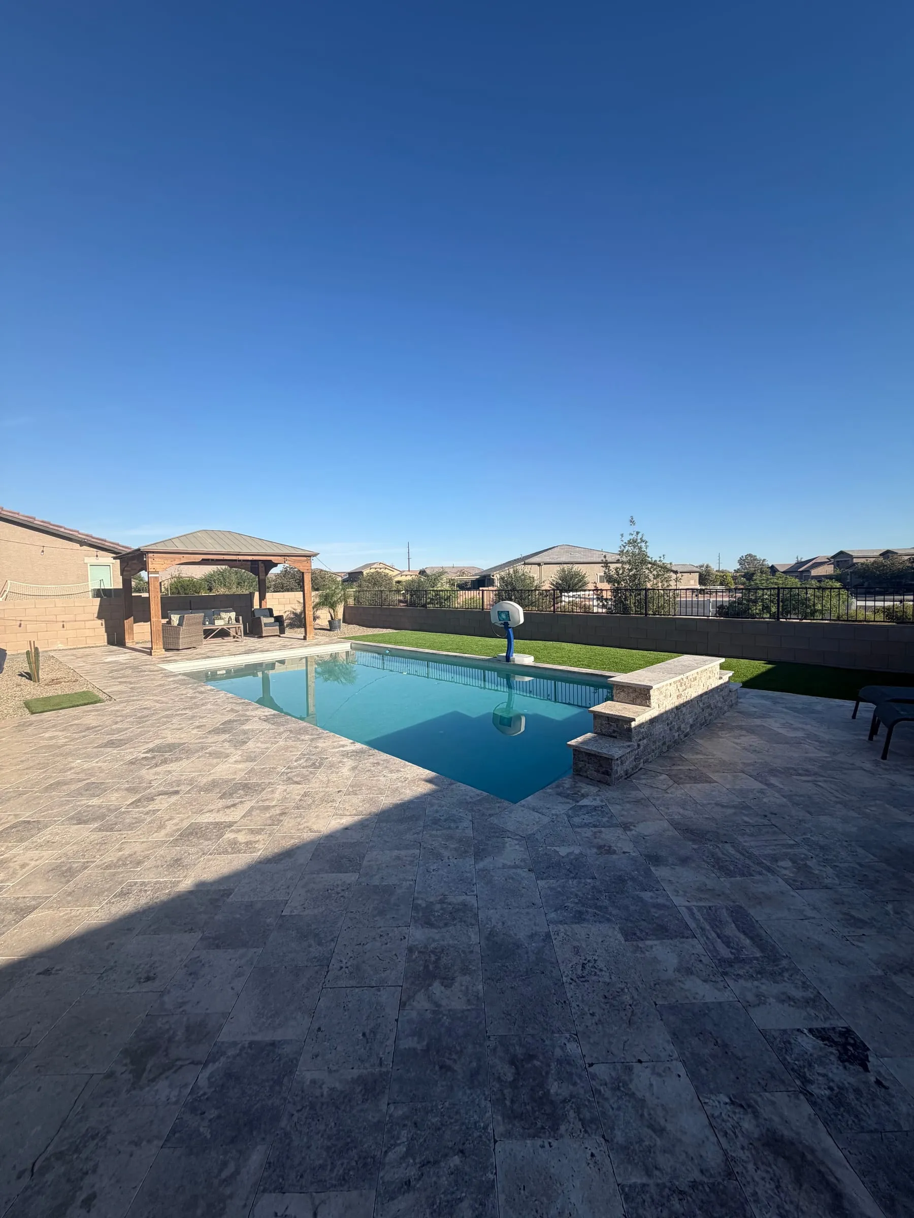 Finished rectangular pool with a stone raised wall and a wide travertine deck in Gladden Farms.