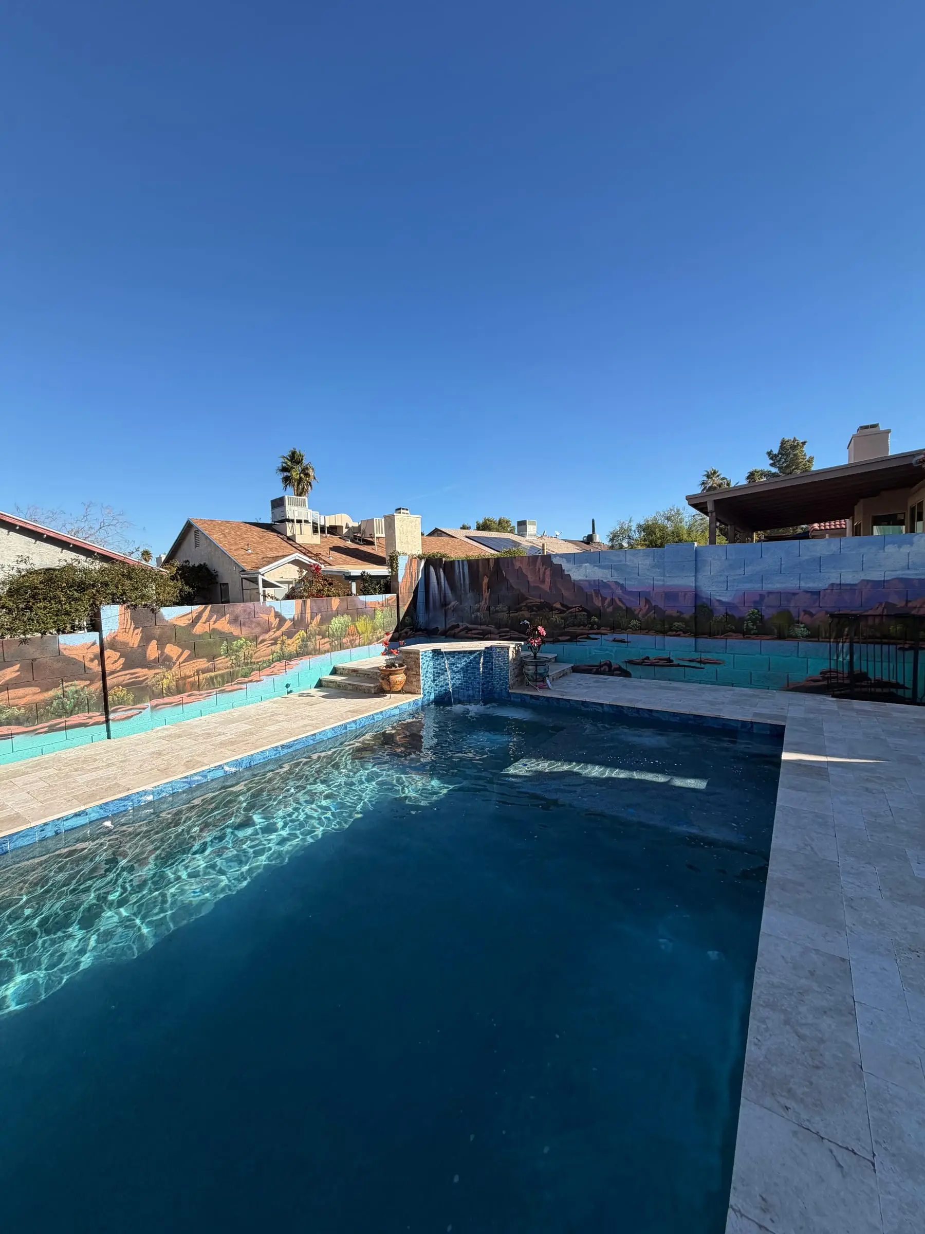 Rectangular pool with a travertine deck inside a backyard enclosed by block walls and fencing in northwest Tucson