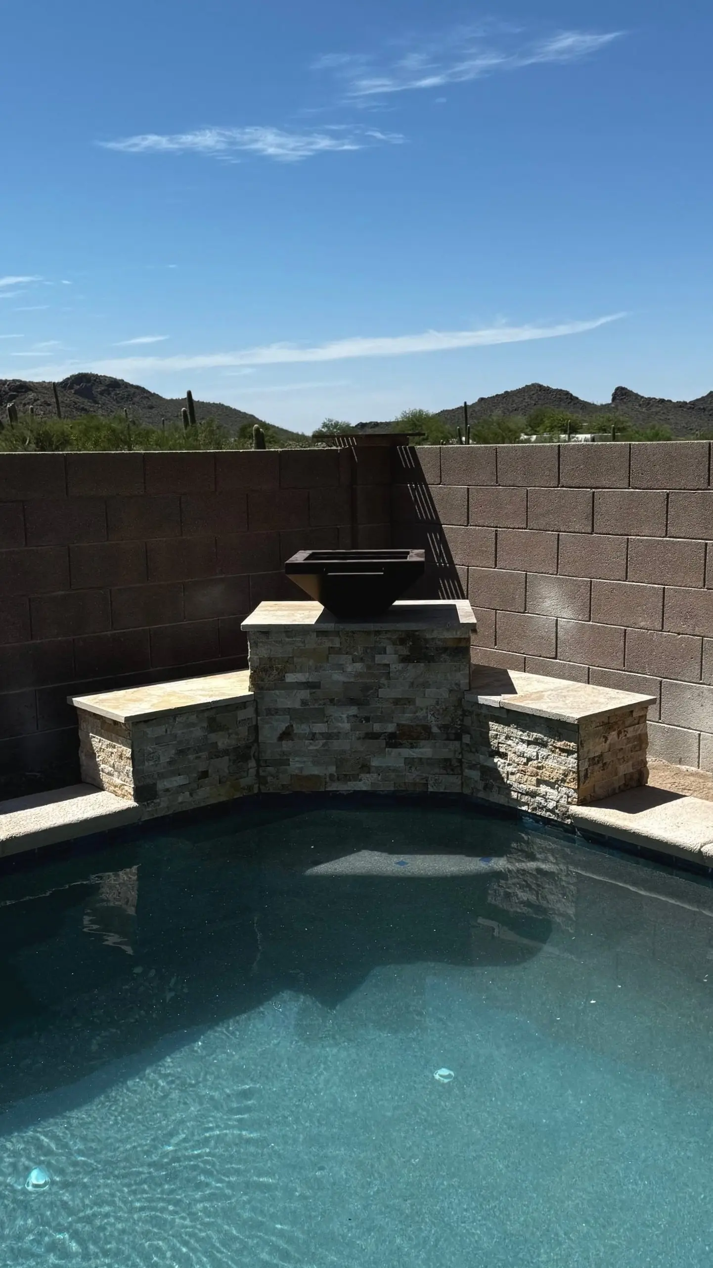 Pool corner with stacked stone raised wall and fire bowl against Tucson desert mountains.