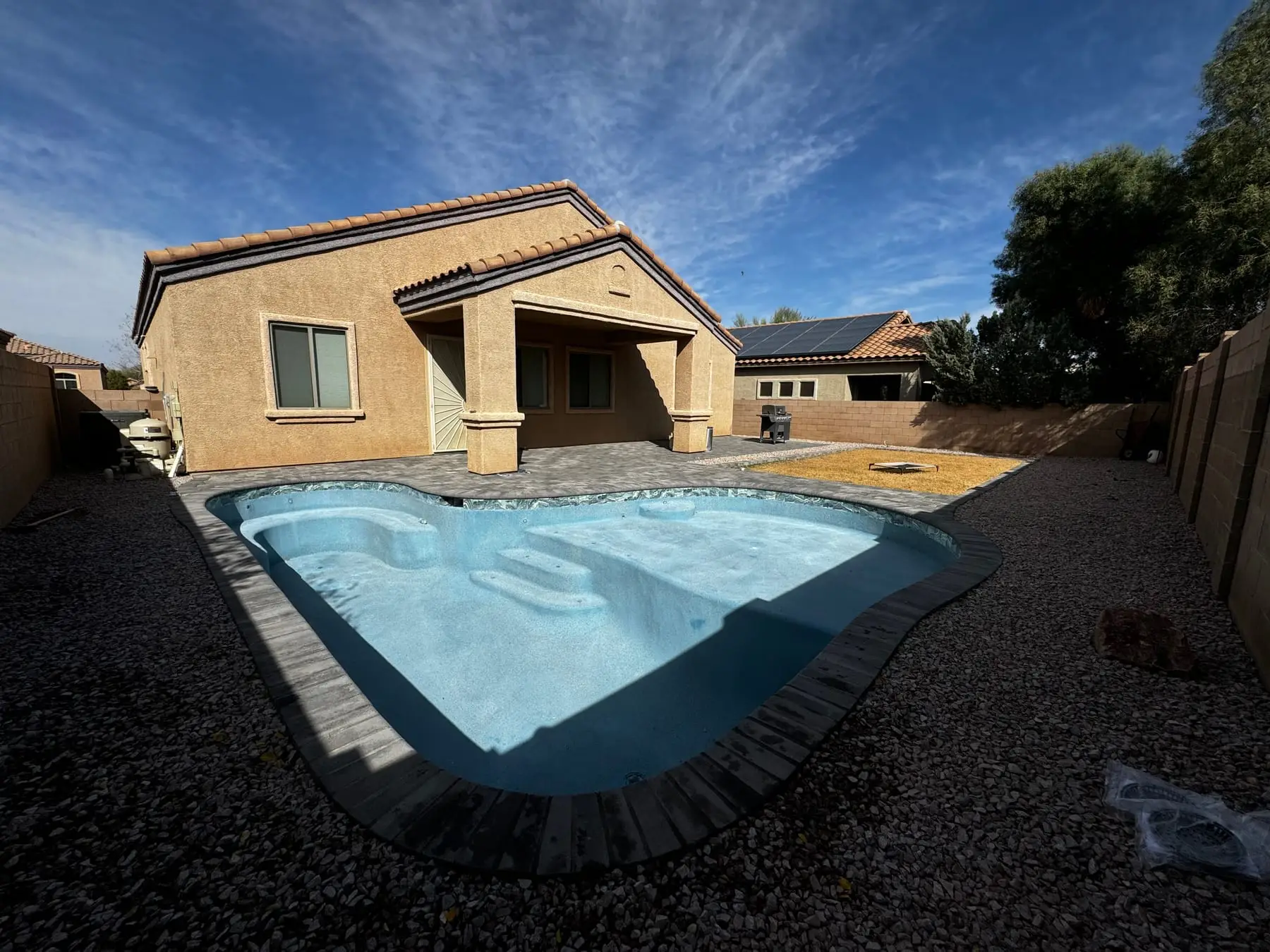 Newly finished freeform pool filling, framed by paver coping and a covered patio.