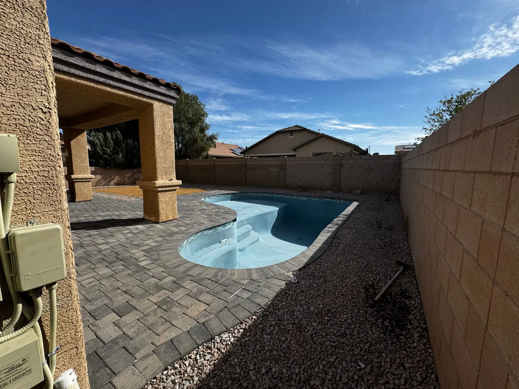 Freeform pool with a fresh light interior finish filling beside a paver deck.