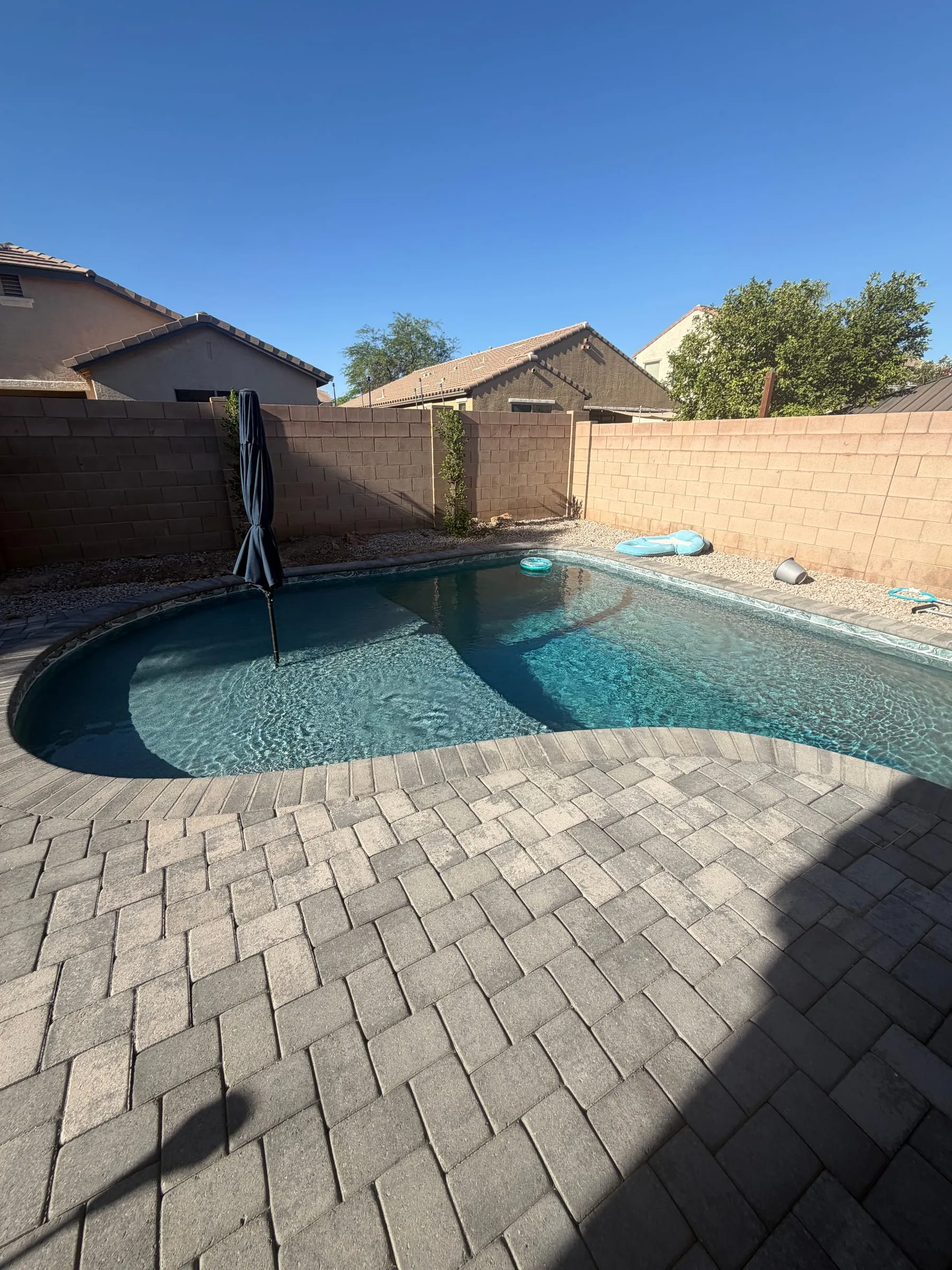 Freeform pool with a gray paver deck inside a backyard enclosed by masonry block walls that form the pool barrier, Marana.