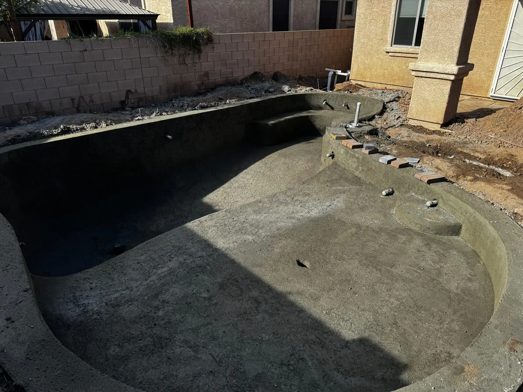 Freeform shotcrete pool shell with curved bench seating and entry steps, Marana, AZ.