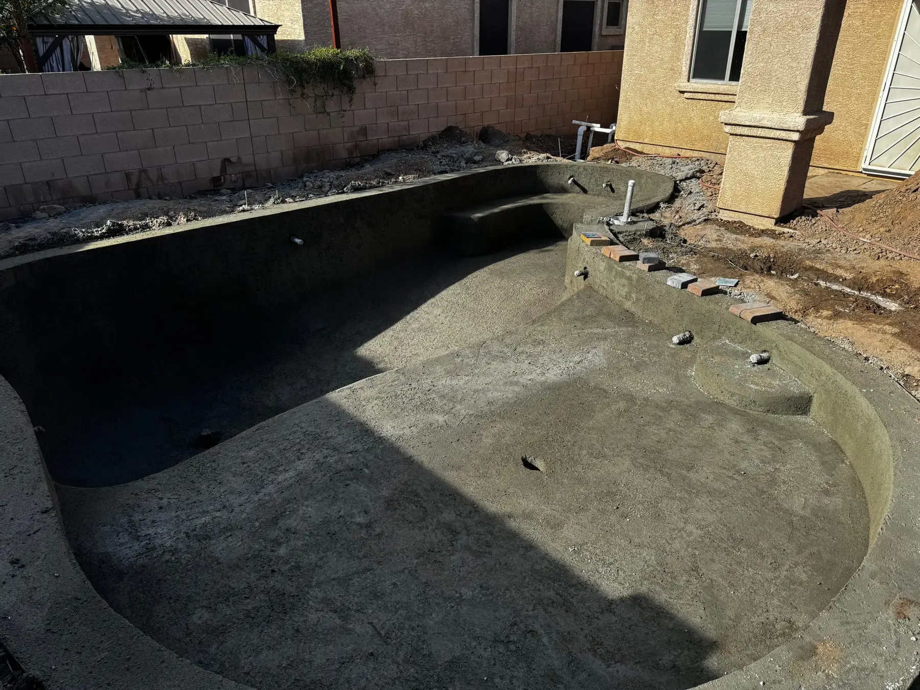 Freeform shotcrete pool shell with curved bench seating and entry steps.