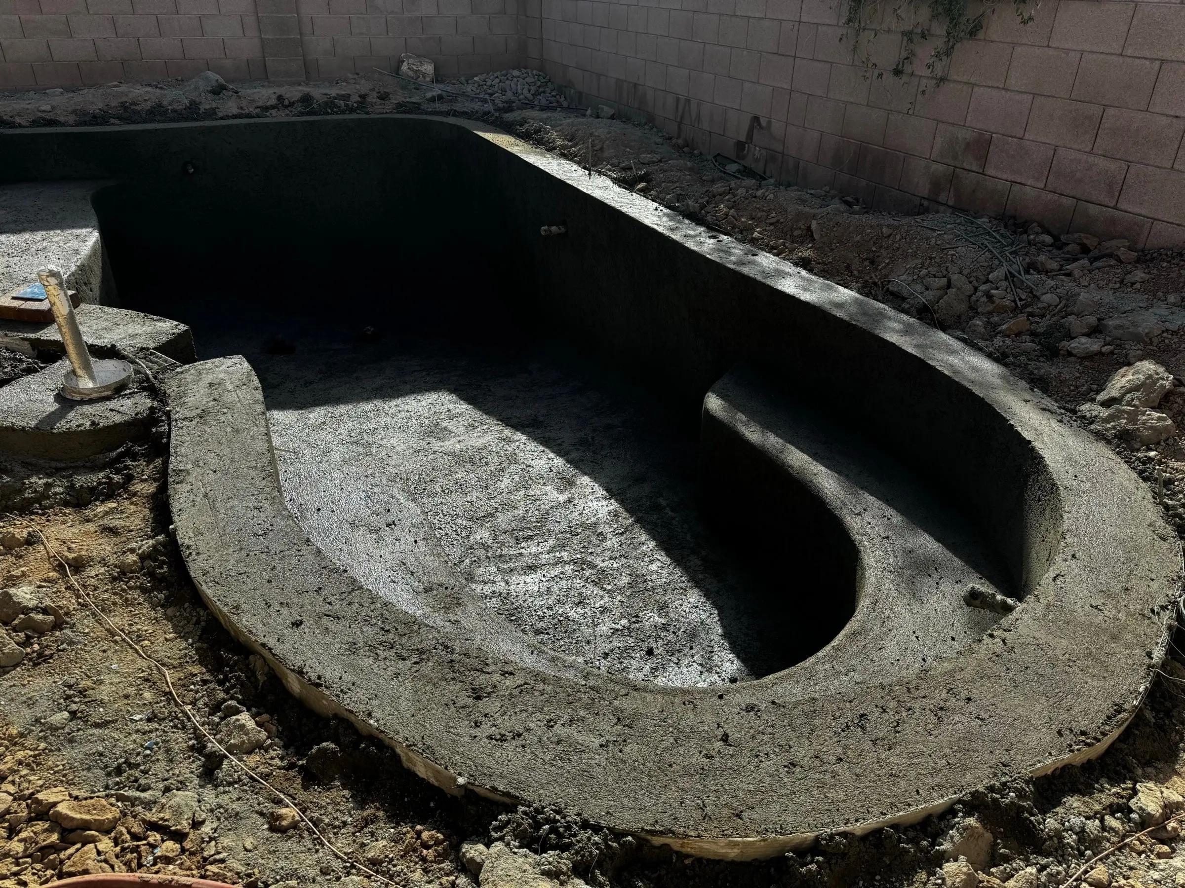Fresh shotcrete shell of a freeform pool showing its curved walls and entry step area.