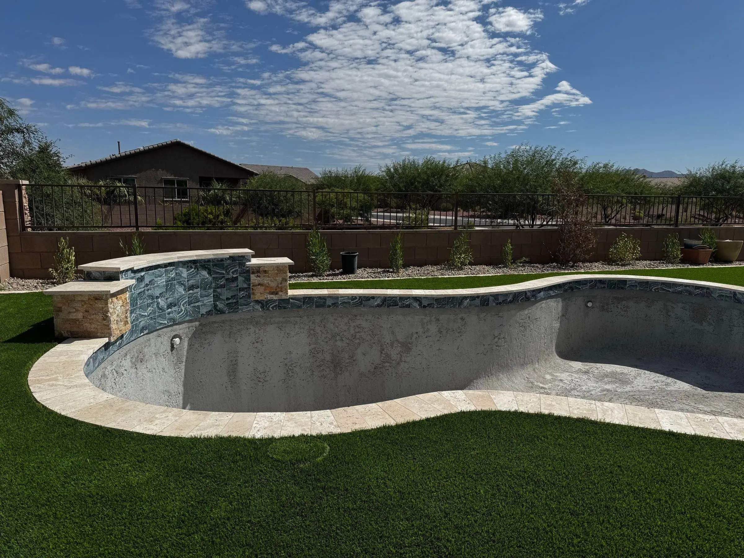 Freeform pool with travertine coping and a stacked stone raised wall, surrounded by new turf, Marana, AZ.