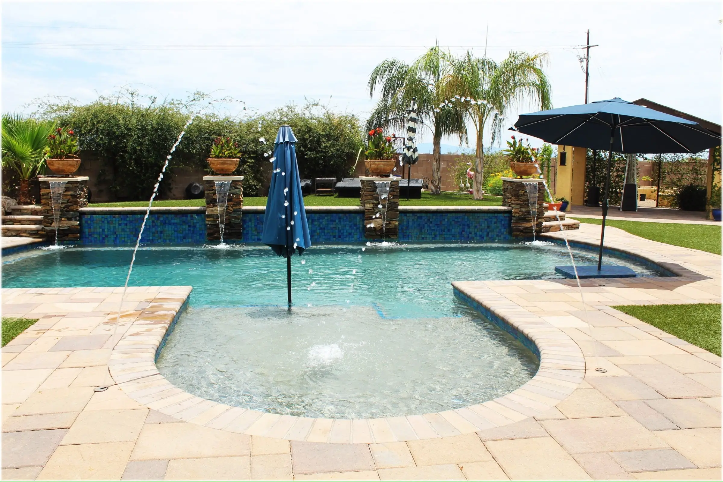 Freeform pool with a rounded tanning ledge, arcing deck jets, sheer descents and paver deck