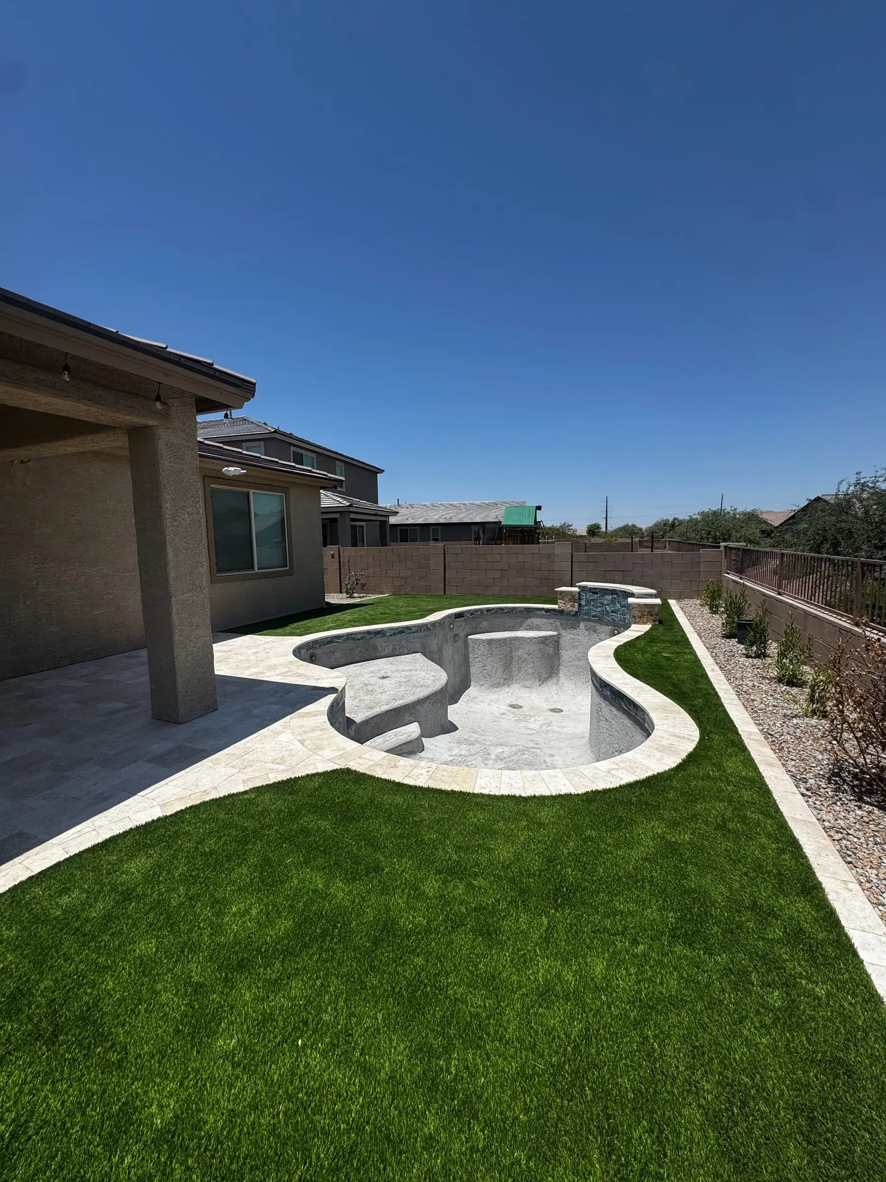 Freeform pool with a fresh interior finish, travertine deck and new turf, ready to fill.