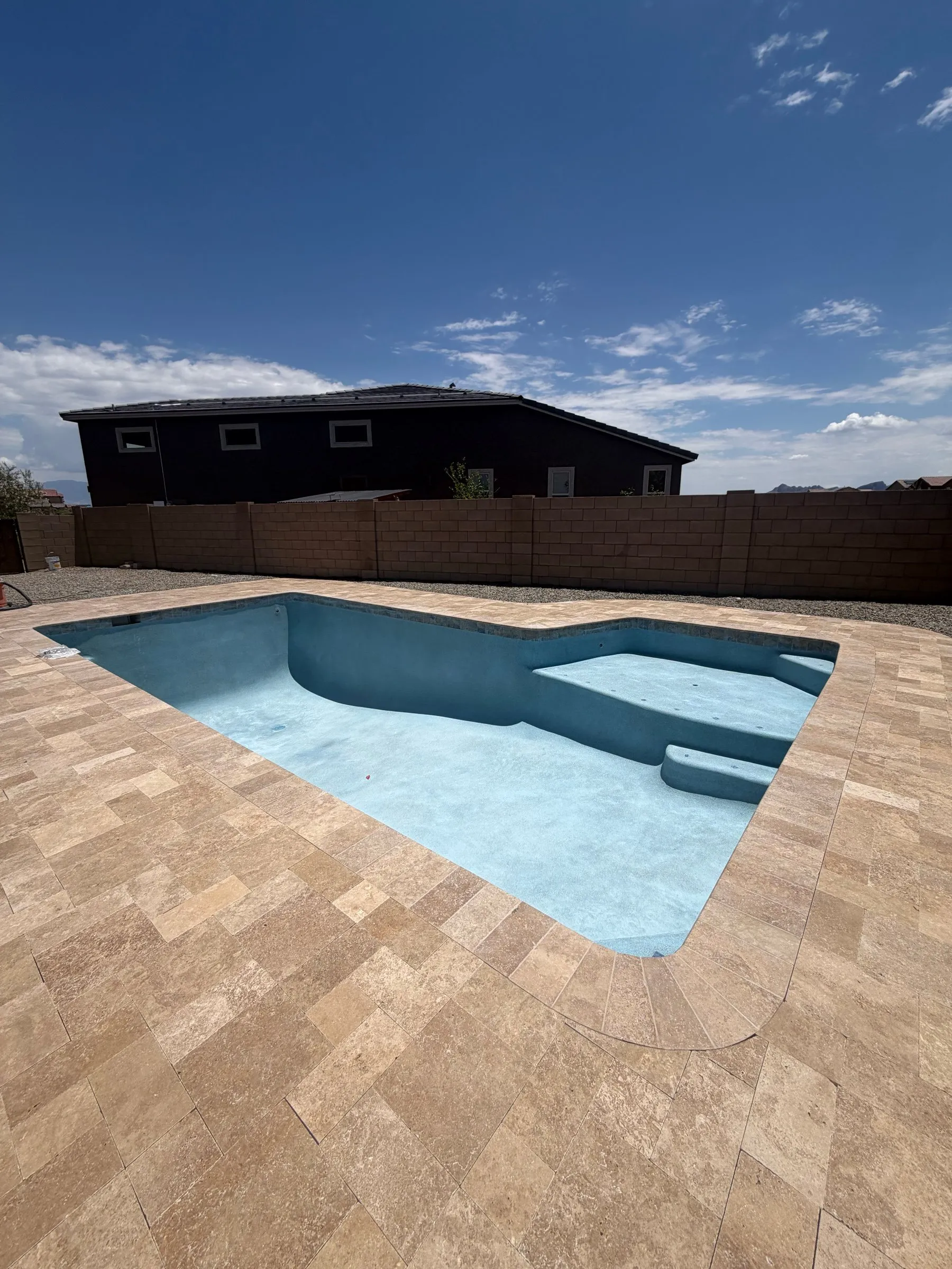 Freshly plastered light blue pool with entry steps surrounded by a tan travertine deck