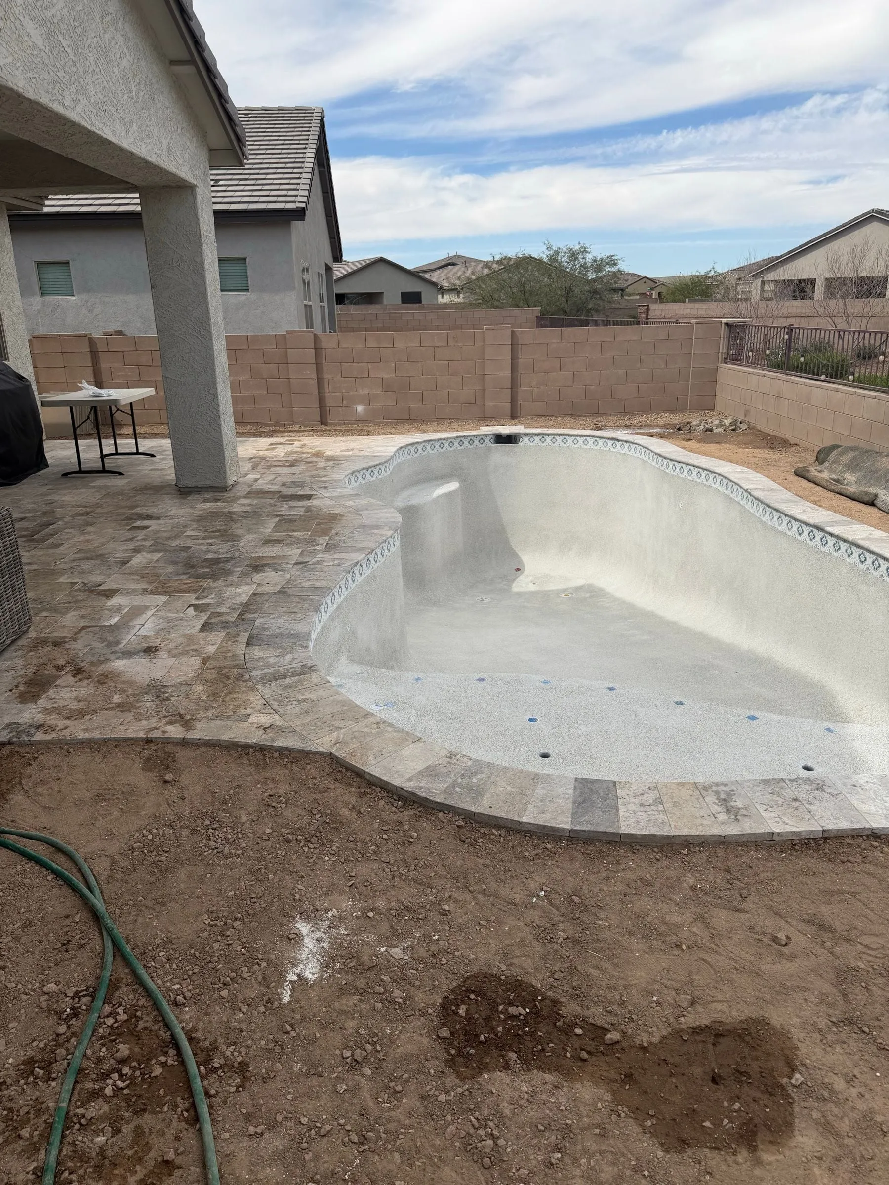 Freshly plastered freeform pool in Marana with travertine coping, waiting to be filled.