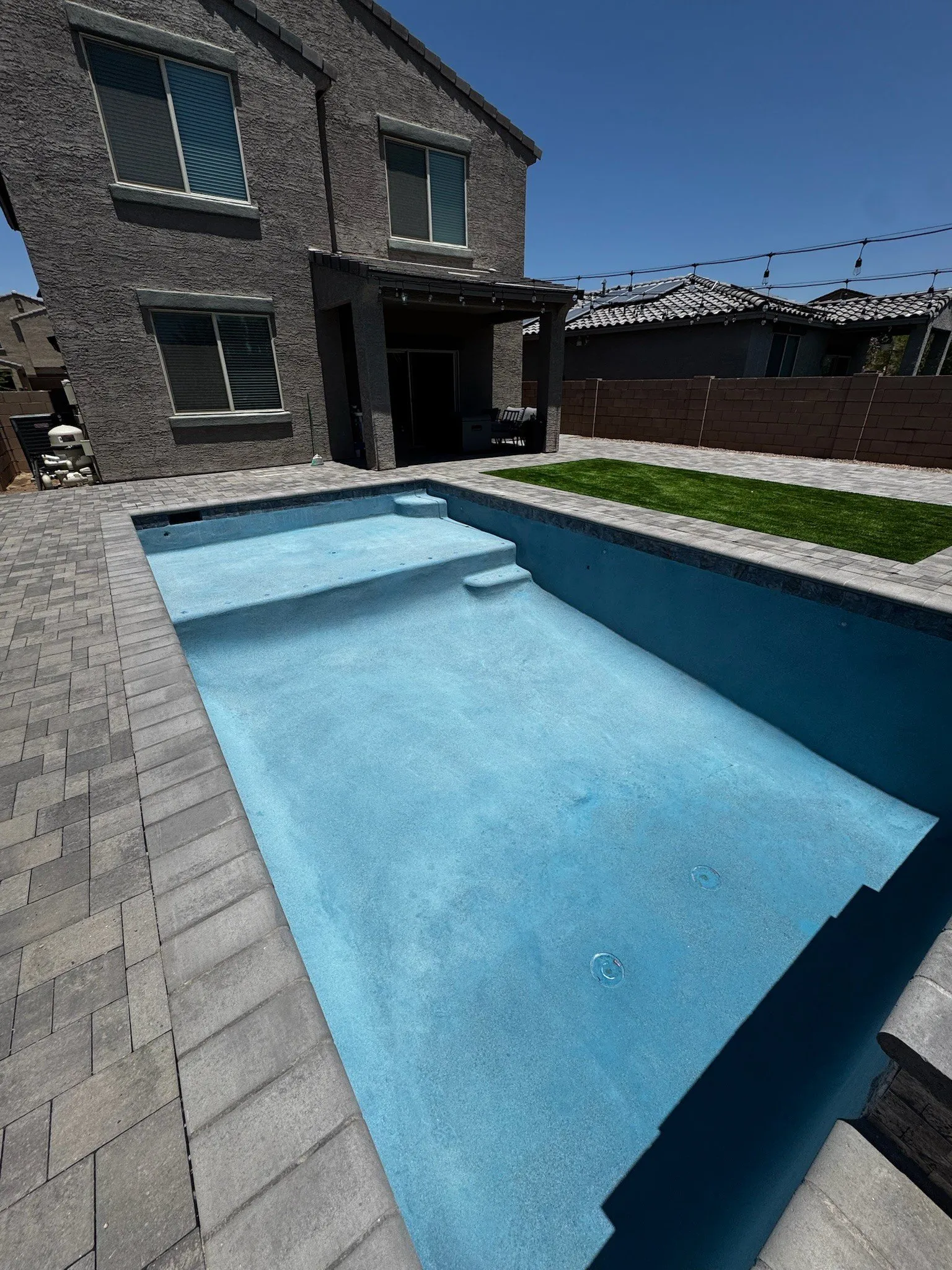 Freshly plastered rectangular pool before filling, with paver deck, entry steps and artificial turf