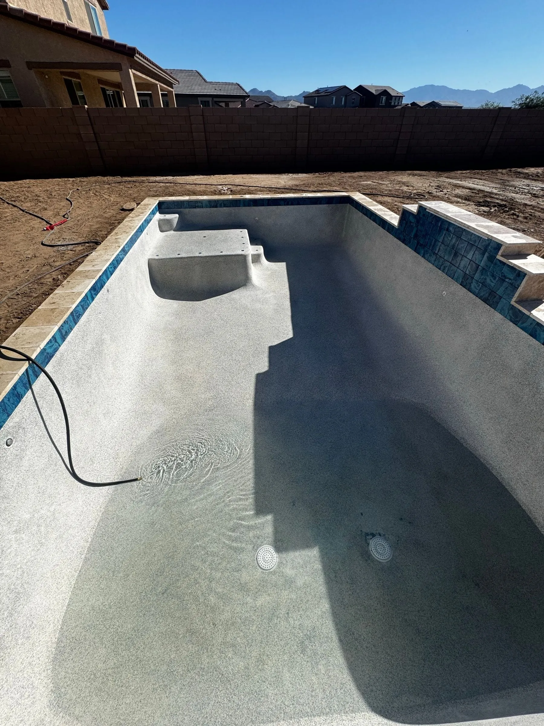 Freshly plastered pool in Marana with a bench, steps and blue waterline tile before filling.