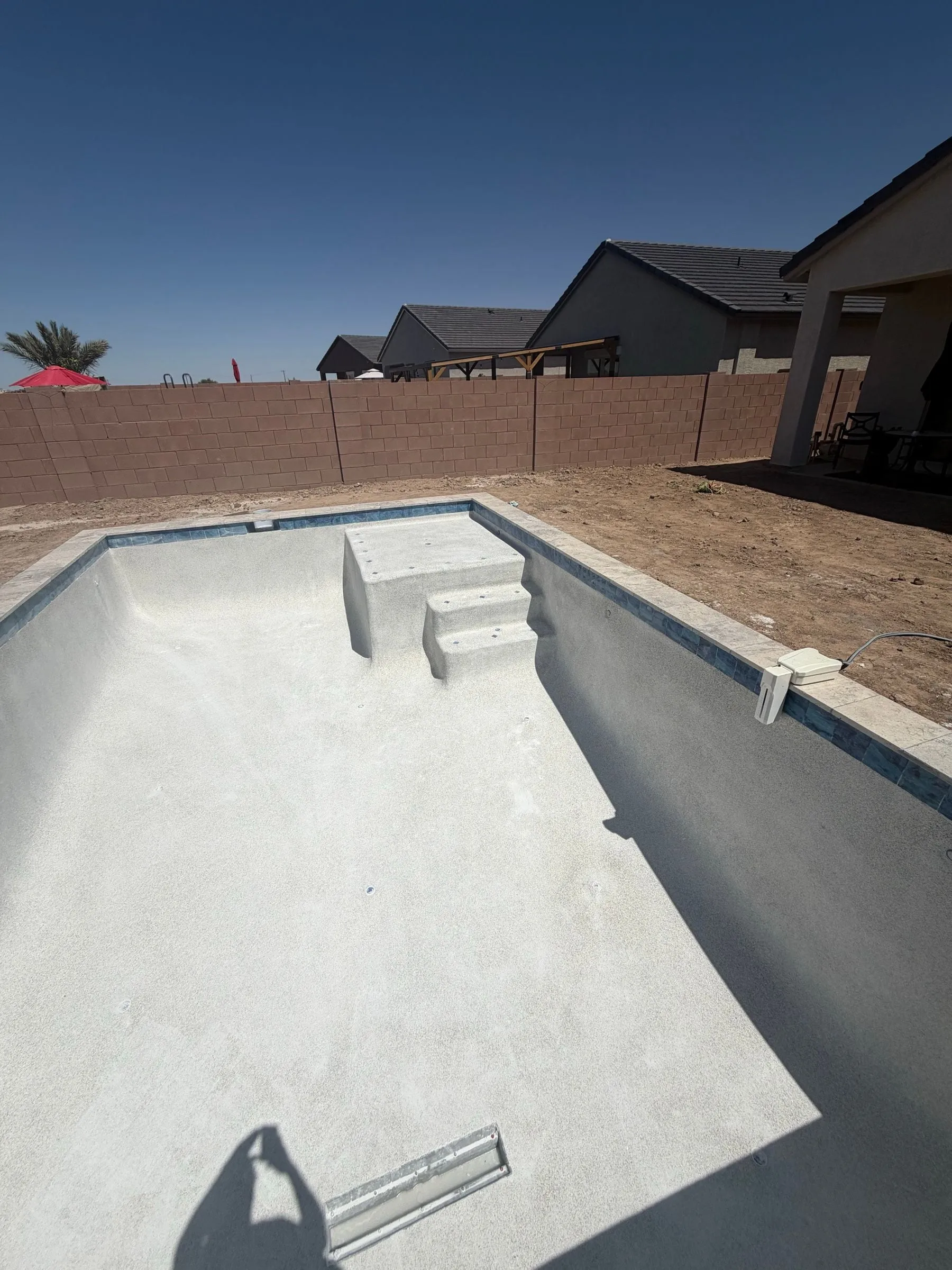 Freshly finished white pool with corner steps and waterline tile before filling.