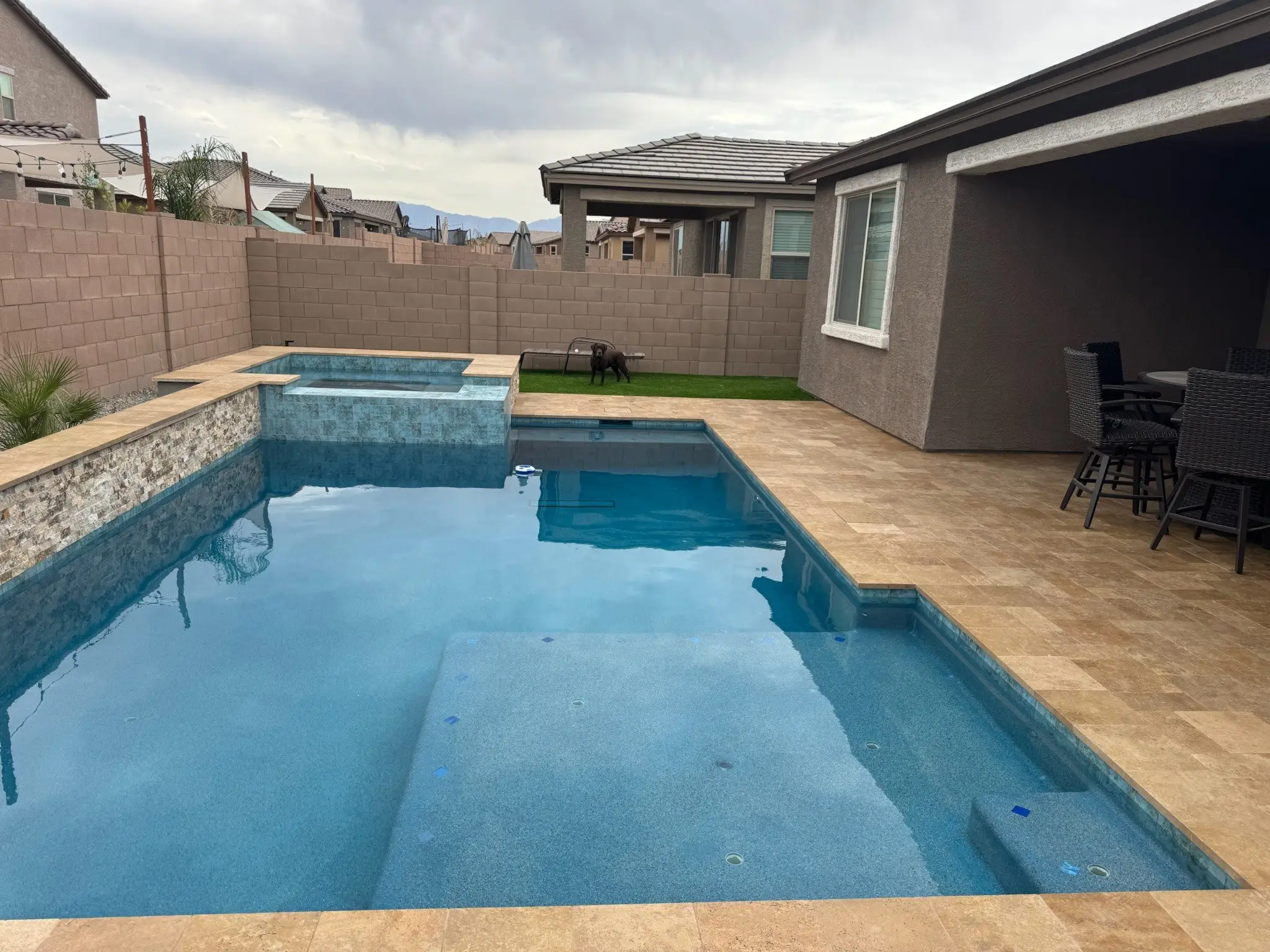 Rectangular pool with tanning ledge, raised spa and stacked stone wall framed by travertine in a Tucson yard.