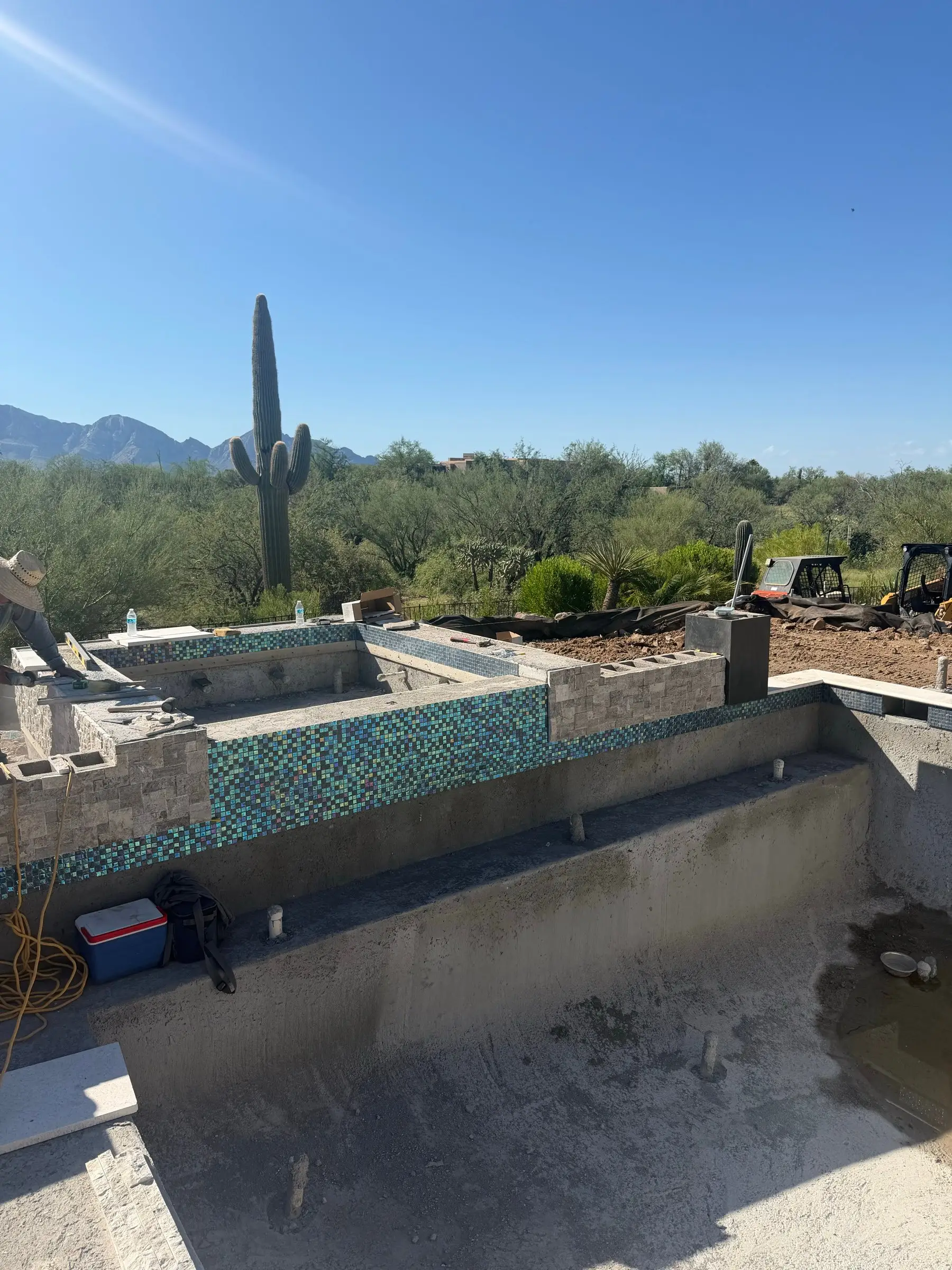 Iridescent glass waterline tile on a raised spa wall above an unplastered pool shell