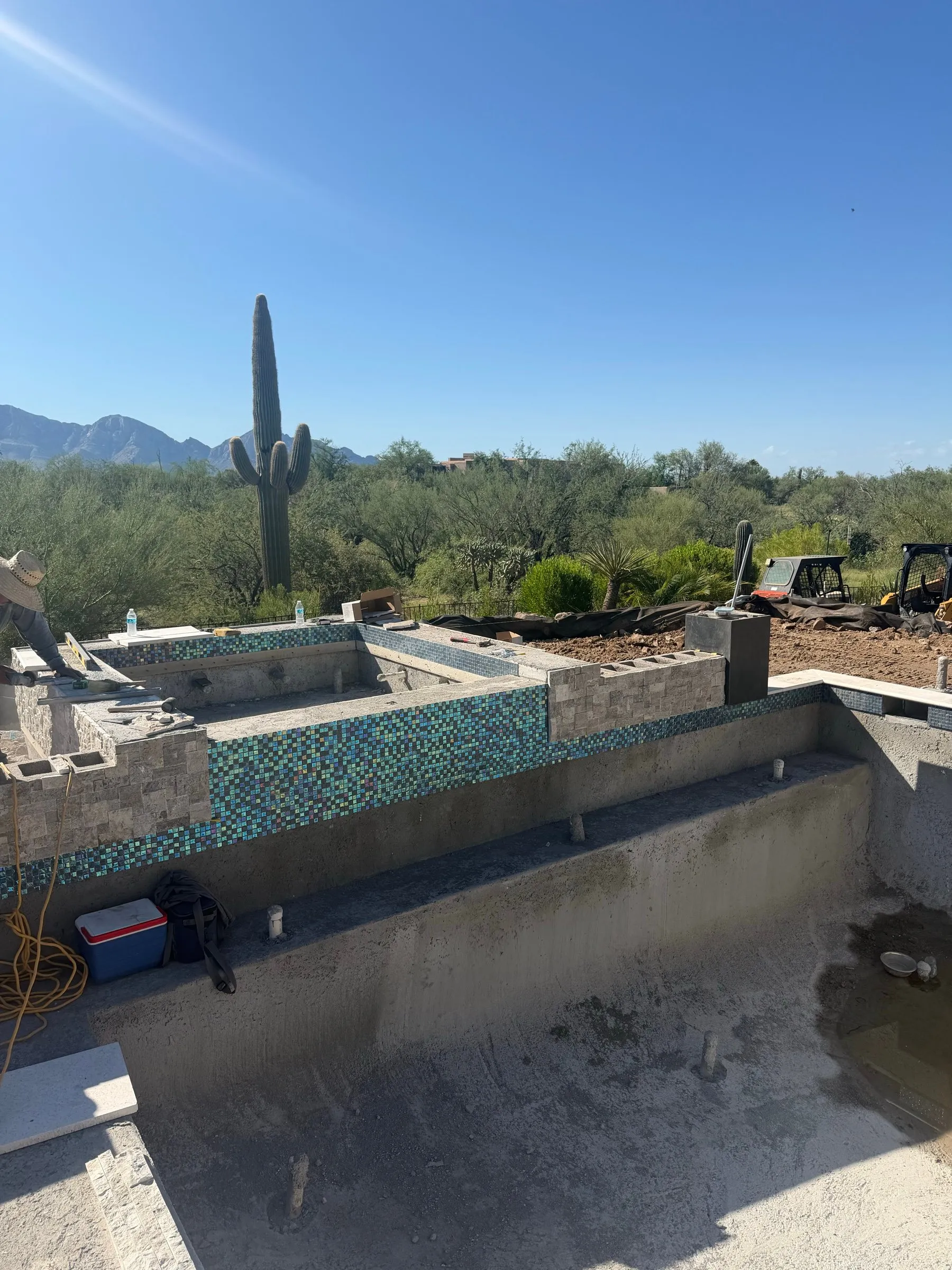 Iridescent glass waterline tile on a raised spa wall above an unplastered pool shell in Dove Mountain.