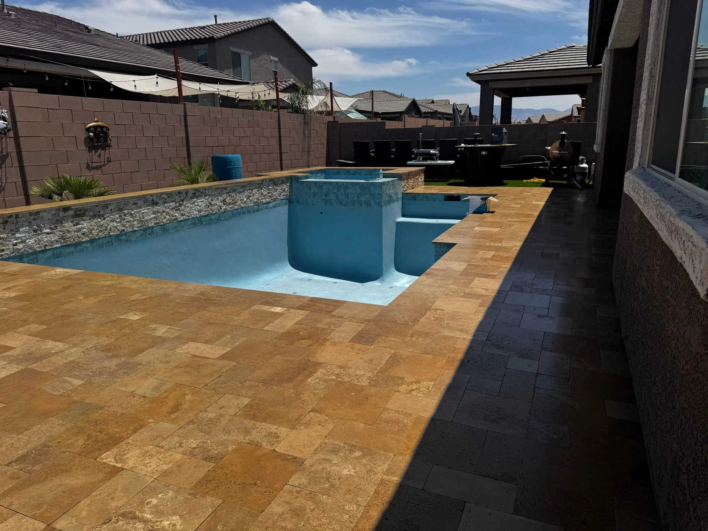 Gold travertine deck around a light blue pool with raised spa and stacked stone wall, Marana, AZ.