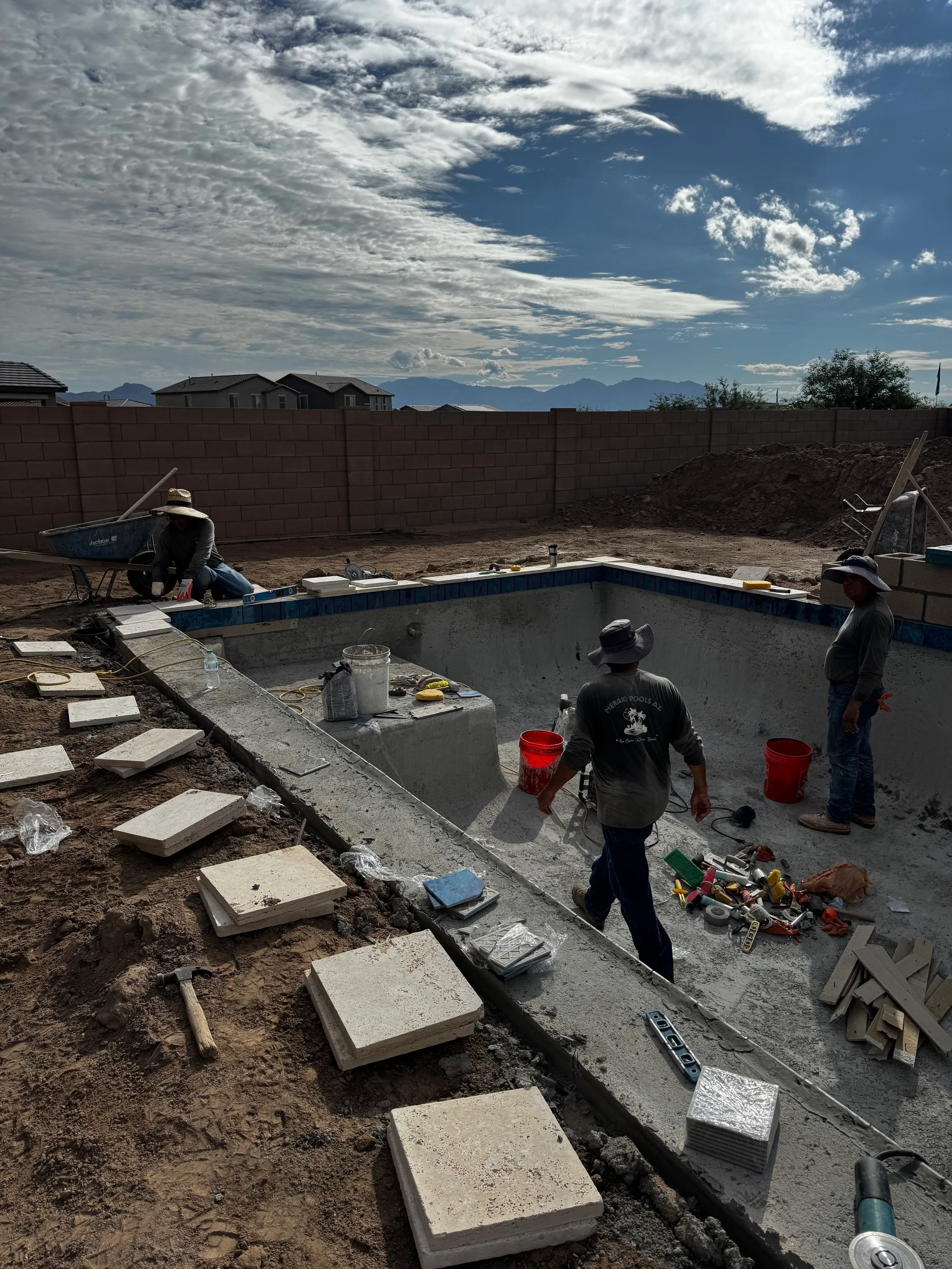 Crew setting waterline tile and coping on a new pool shell during construction
