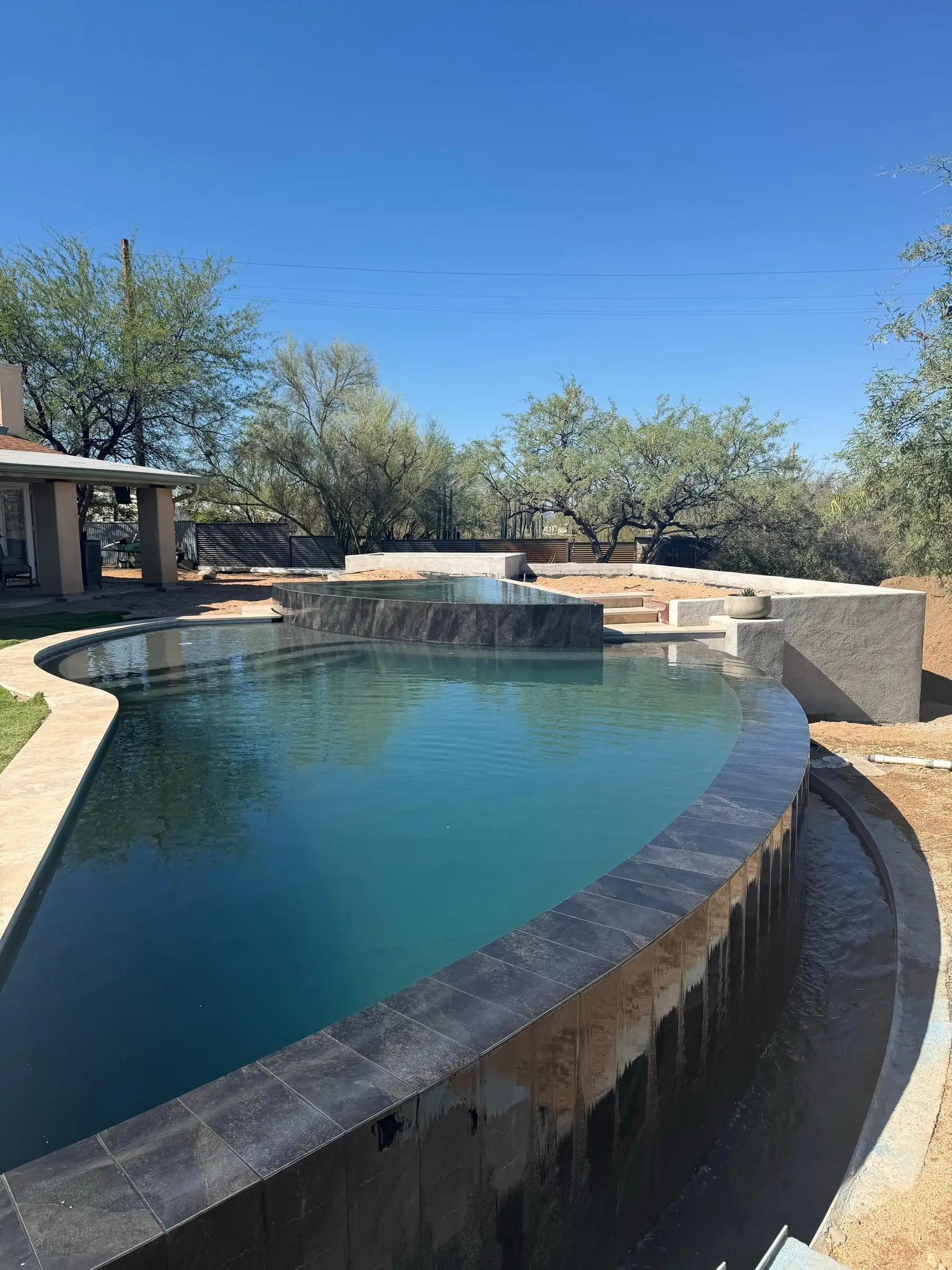 Finished infinity-edge pool in the Oro Valley area with a curved vanishing edge, dark tile and raised spa