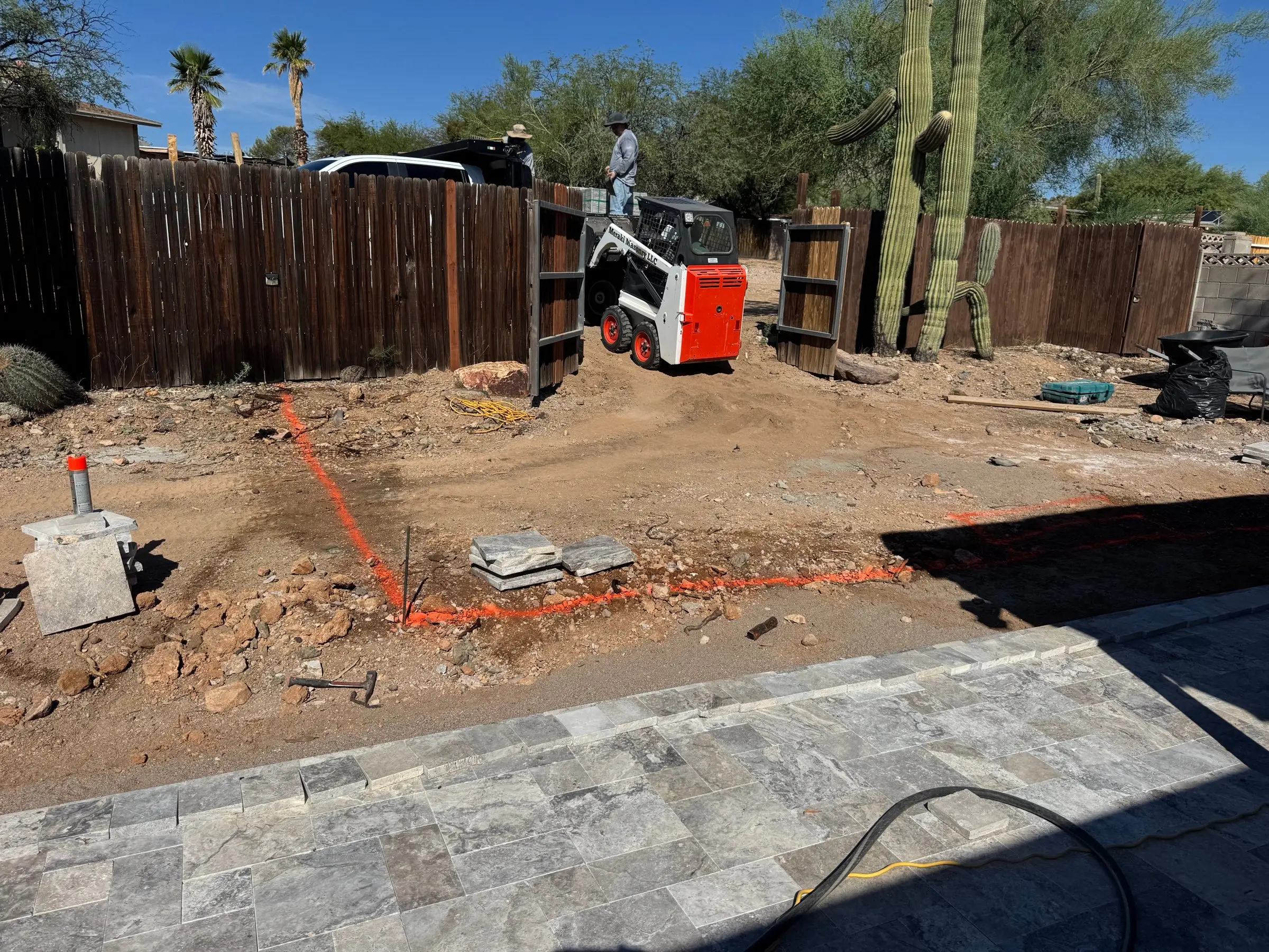 Orange layout paint marking a new area beside a travertine deck with skid steer