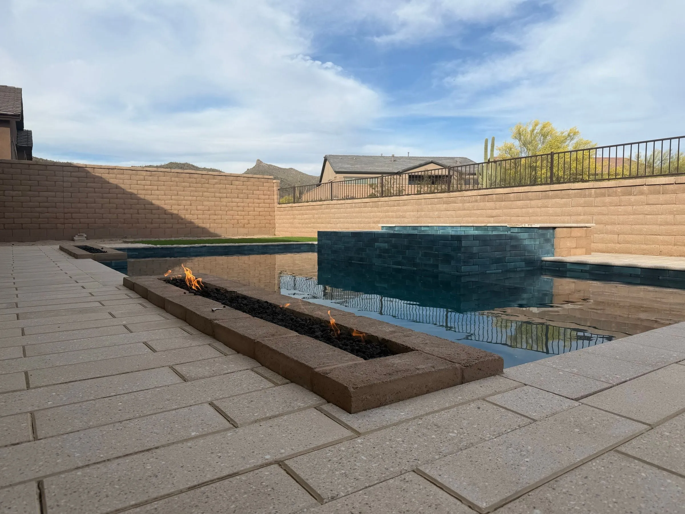 Linear fire trough burning beside a pool in Marana, with a dark-tiled raised spa beyond.