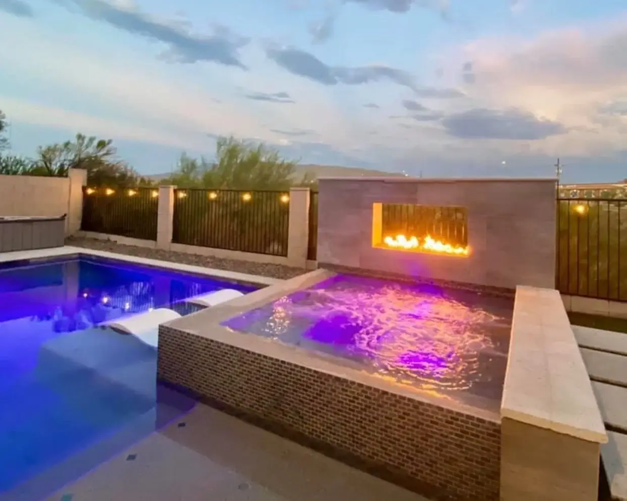 Raised spa with purple lighting beside a linear fire wall and pool tanning ledge at dusk in Arizona.