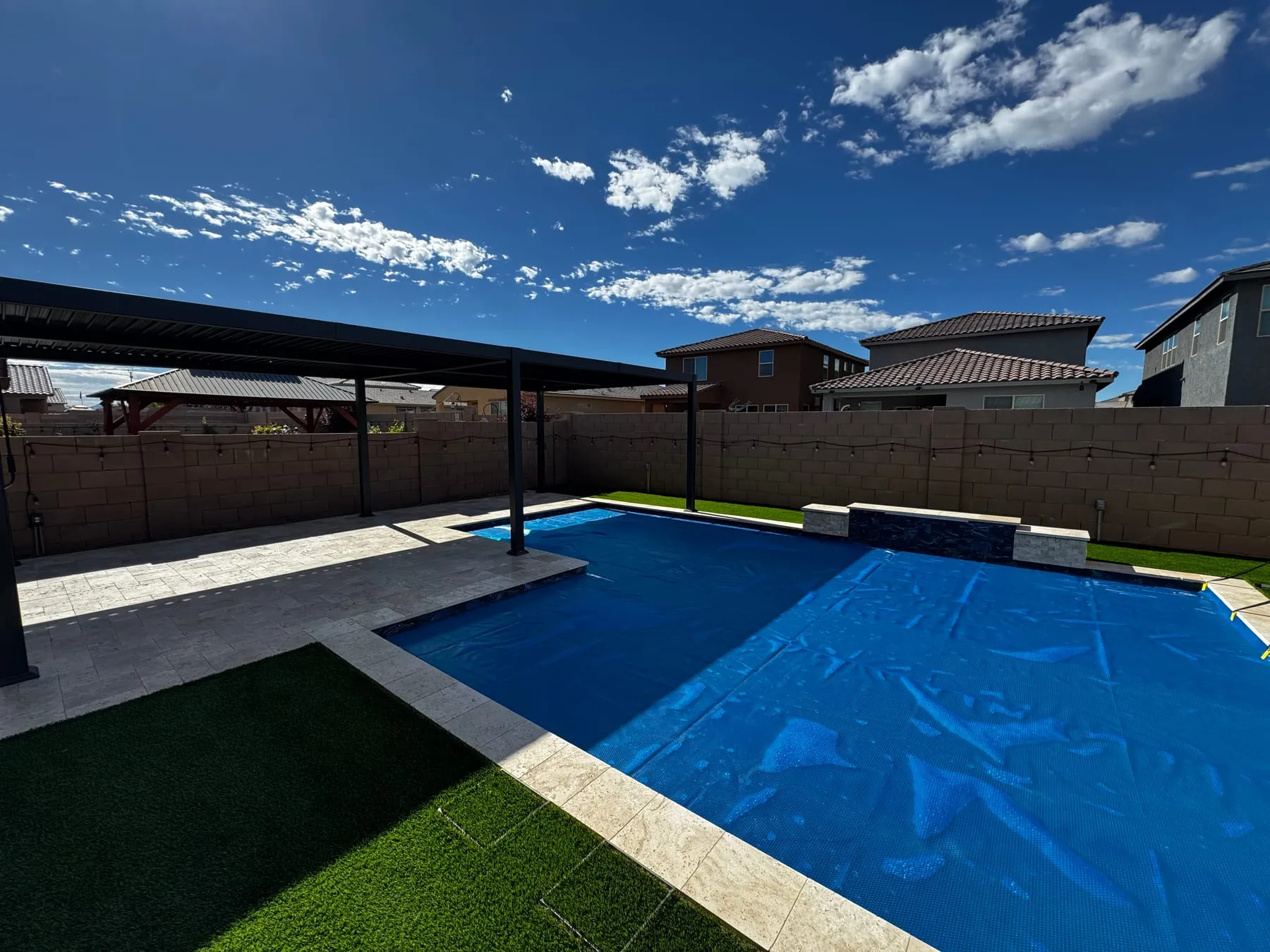 Louvered pergola shading a travertine pool deck beside a new pool and artificial turf in southeast Tucson.