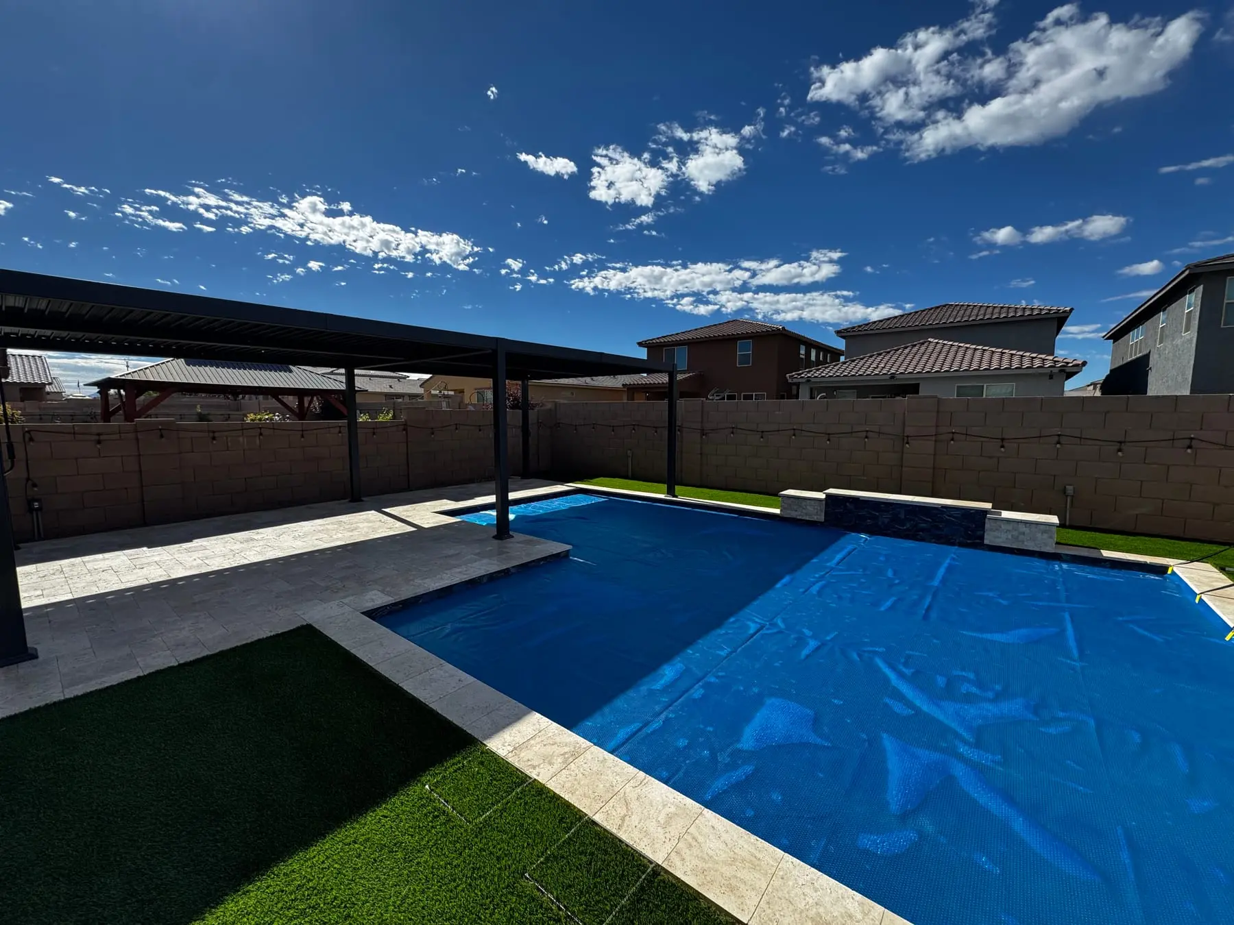 Louvered pergola shading a travertine pool deck beside a pool under a solar cover, with turf, southeast Tucson, AZ.
