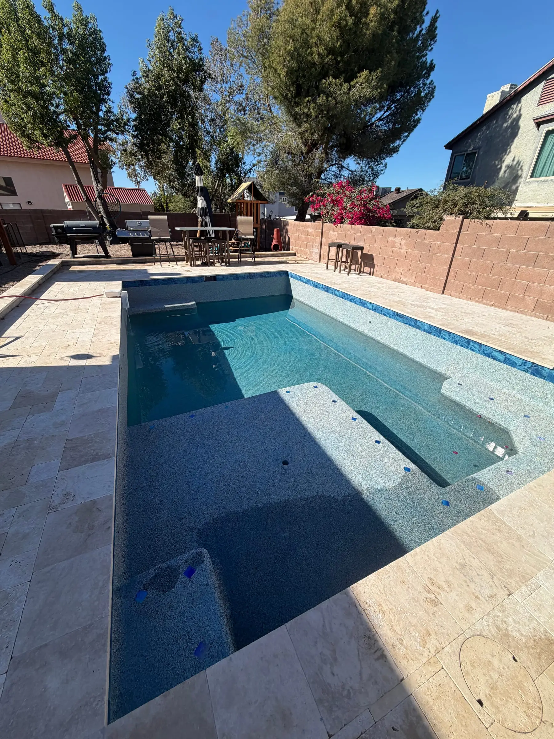 New pool with a blue interior finish filling beside a travertine deck, northwest Tucson, AZ.