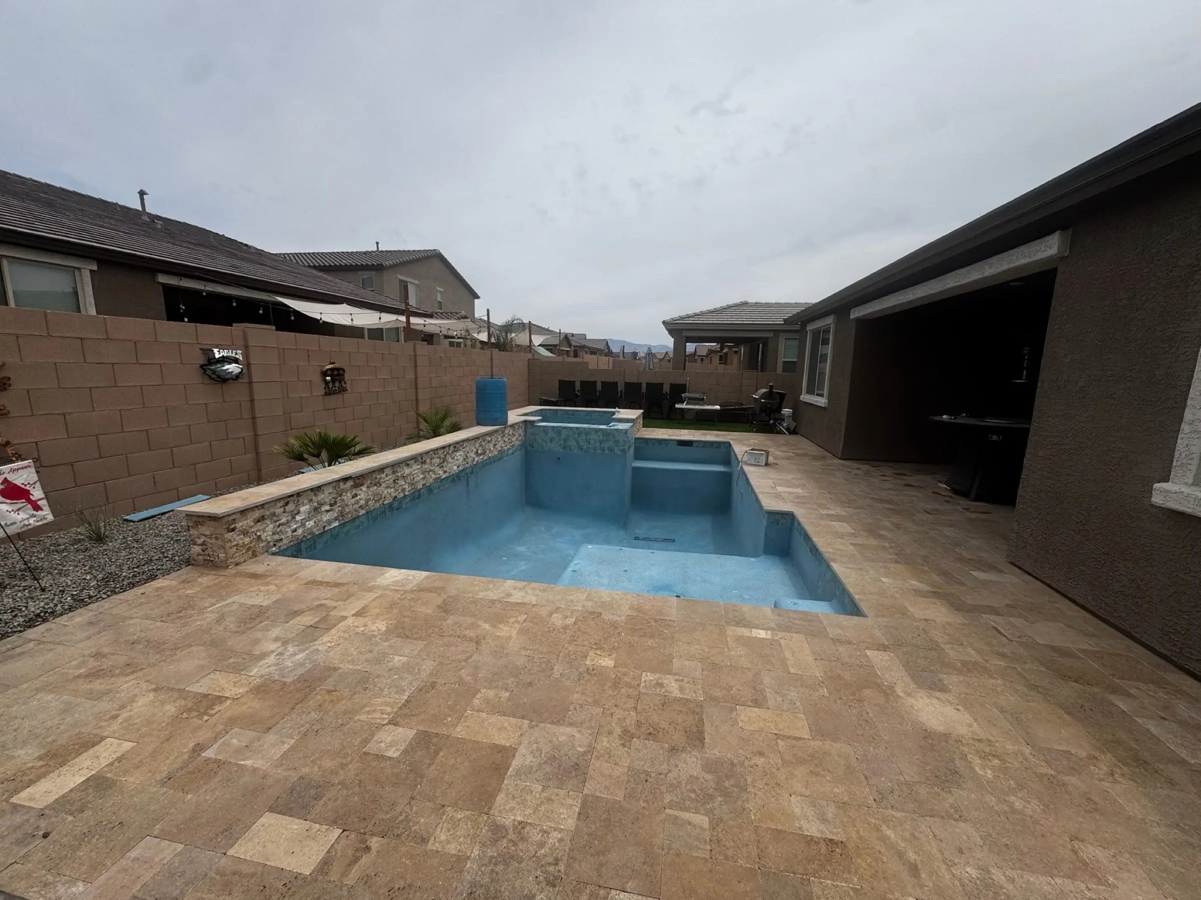 Newly plastered pool filling with water beside a raised spa wall and travertine deck