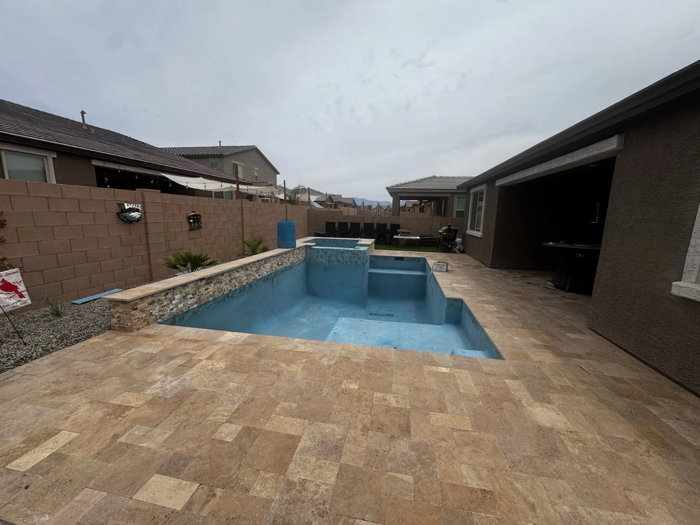 Newly plastered pool filling with water beside a raised spa wall and travertine deck.