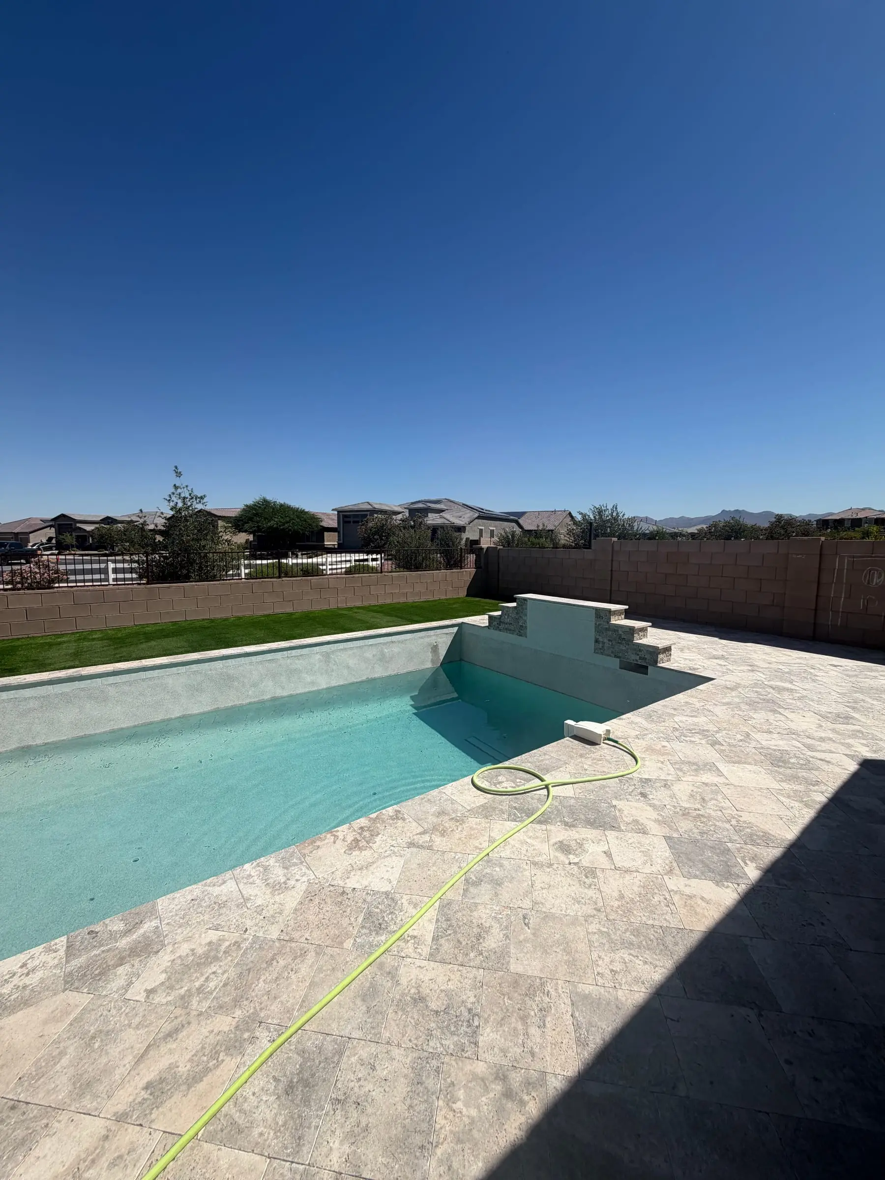 Newly finished pool filling with water beside a travertine deck and a stone raised wall, Gladden Farms in Marana, AZ.