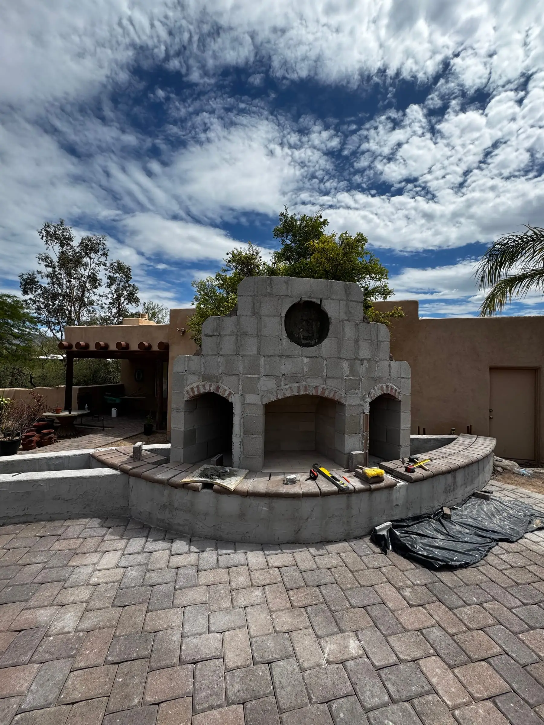 Outdoor fireplace with three openings and a curved seat wall on a new paver patio.